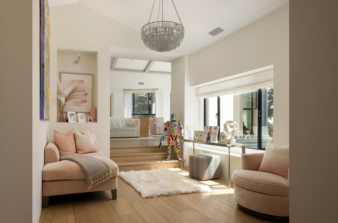 At the entrance to the suite, a small lounge features a built-in window seat and a pair of soft blush-toned chairs frame the space, while a narrow console beneath the window adds a gallery-like layer.