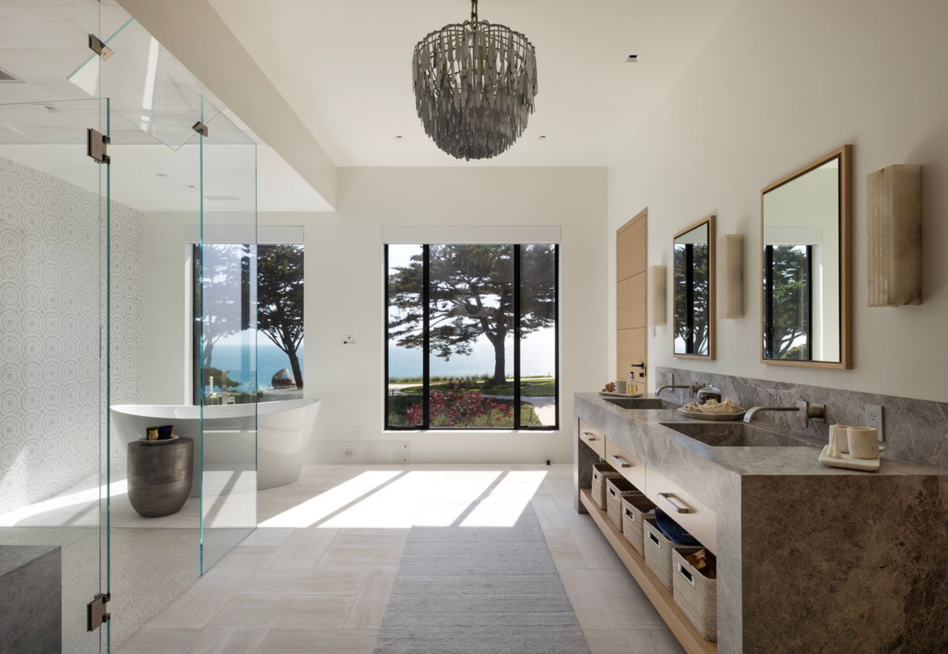 The bathroom continues the same open, airy approach, with a double vanity stretching along one wall beneath two mirrors and a hanging chandelier centered above the room. 