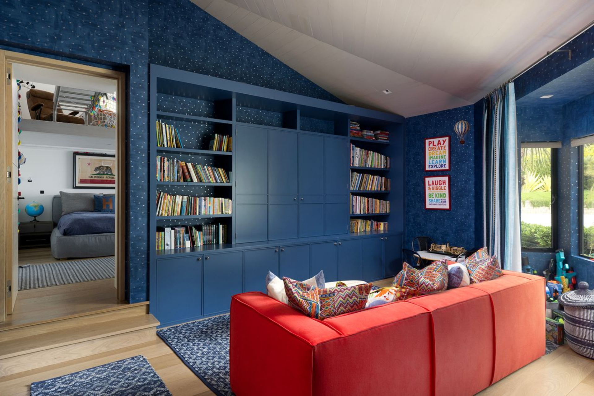 One of the rooms combines a bedroom and a library, with deep blue walls and matching built-in cabinetry running across the main wall. 