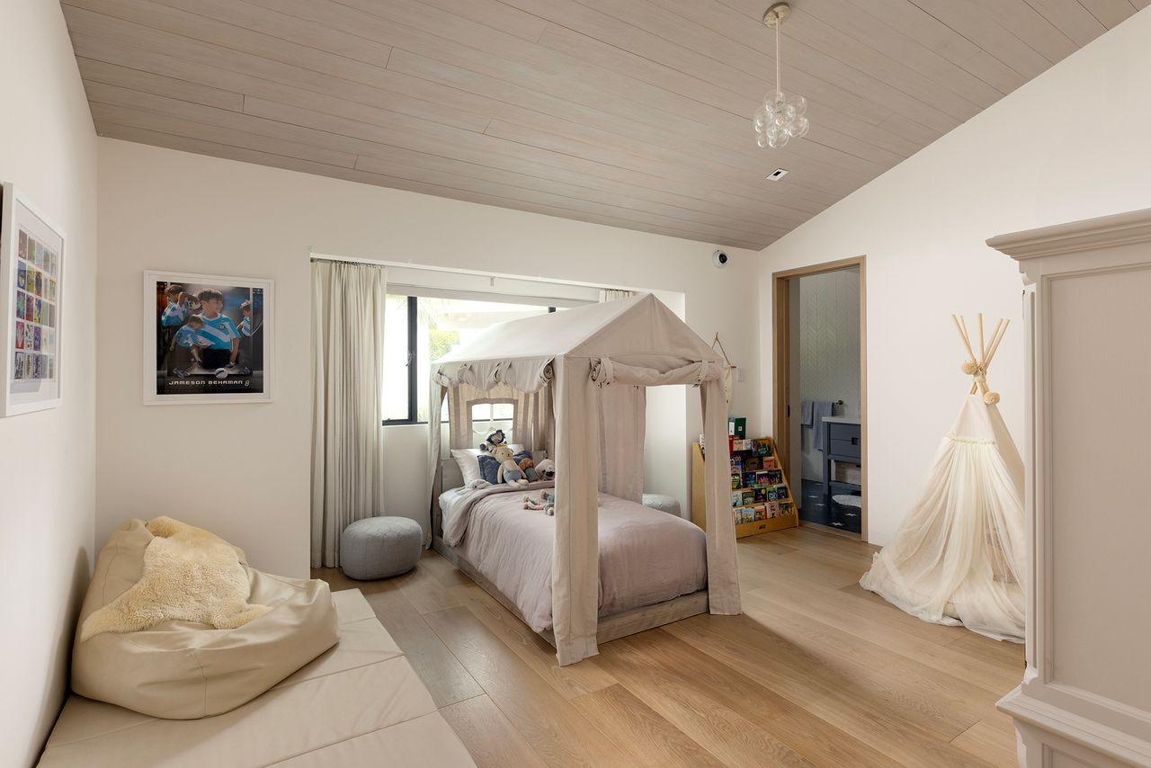 The second room shifts to a softer look, with pale walls, light wood floors, and a canopy bed positioned near the center of the space. 