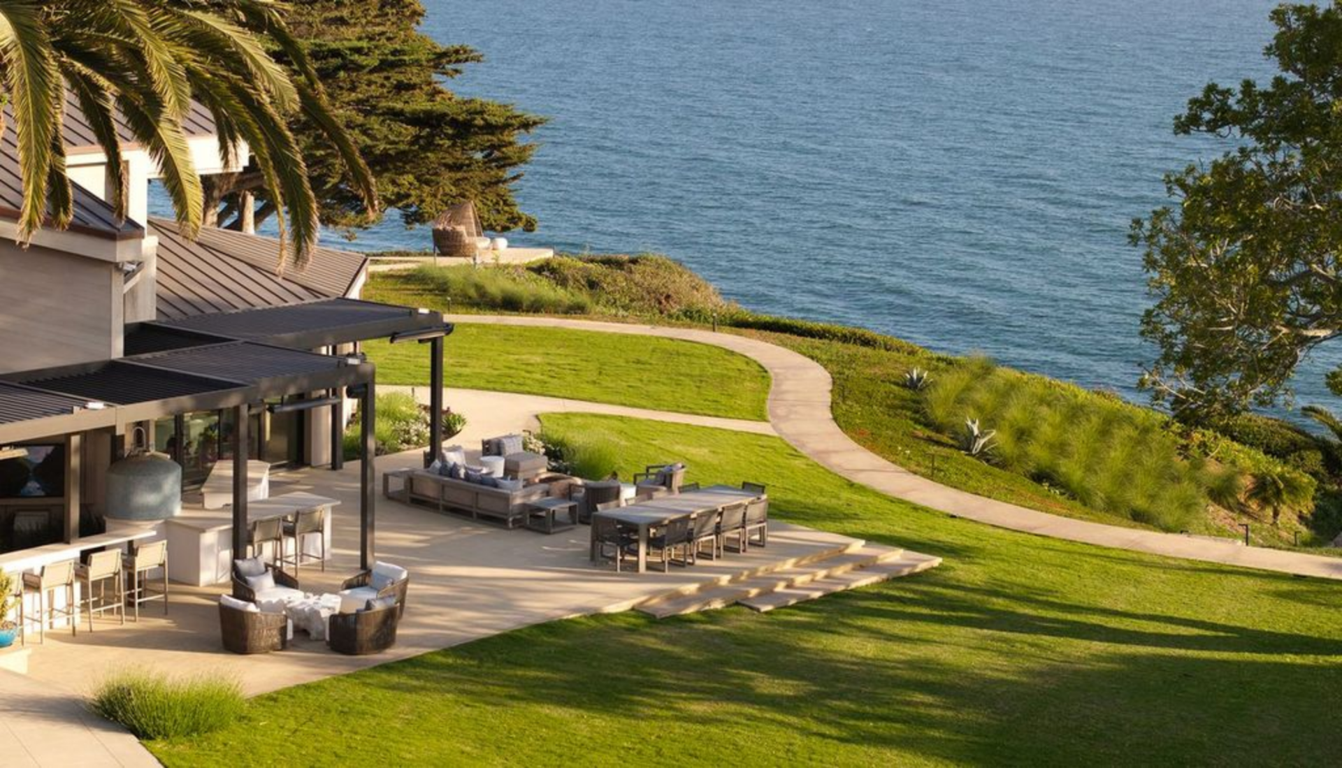 A built-in grill and bar seating run along one side, with a larger dining table and lounge seating arranged on the edges of the patio.