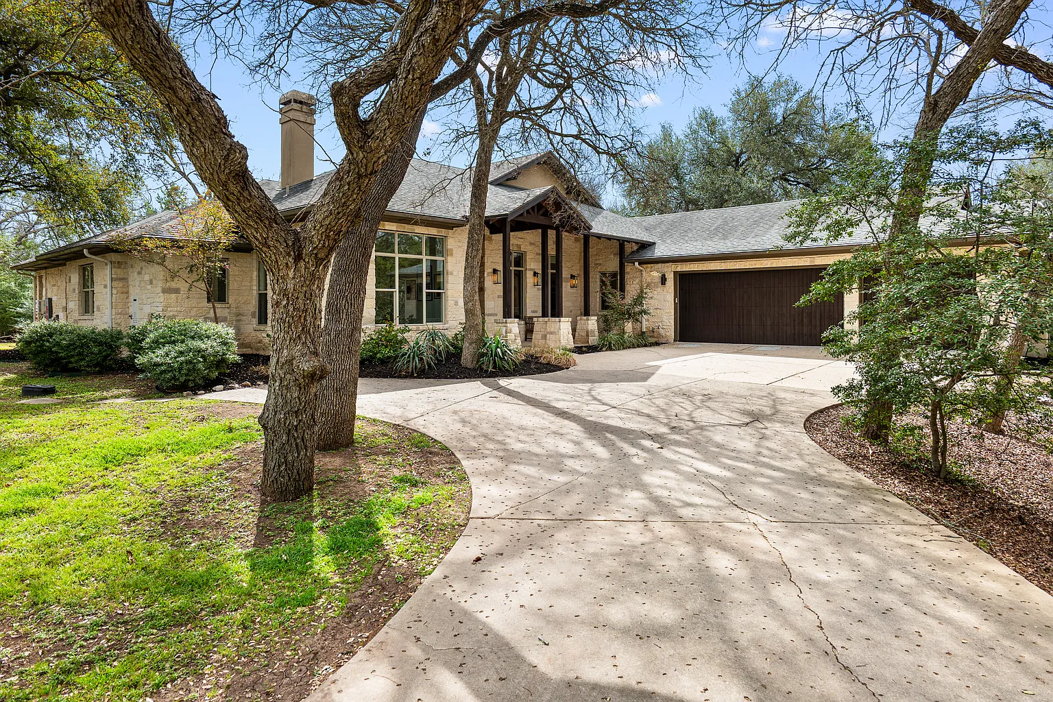 Wide driveway leads to a neutral stoned home with a covered porch.