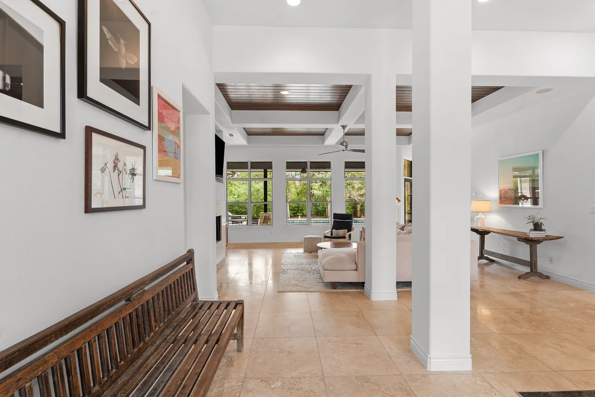 Straight ahead, the layout begins to open into the main living spaces, where the limestone continues, and the ceiling shifts into more detailed treatments with recessed sections framed in dark wood.