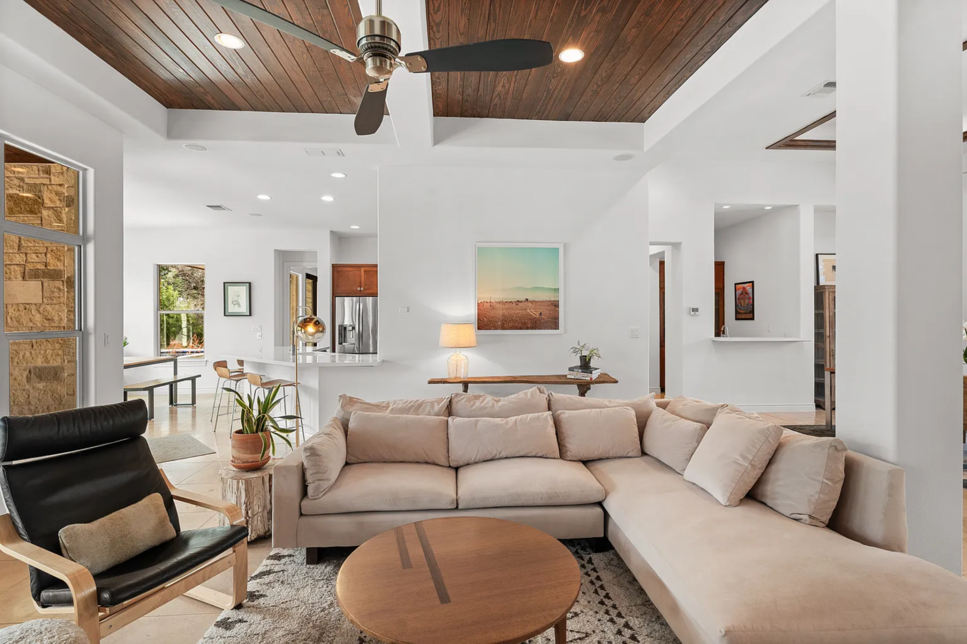 Straight ahead, the entry opens directly into the main living room, where the seating is arranged at the center with a large sectional, a round wood coffee table, and a black lounge chair positioned near the windows. 