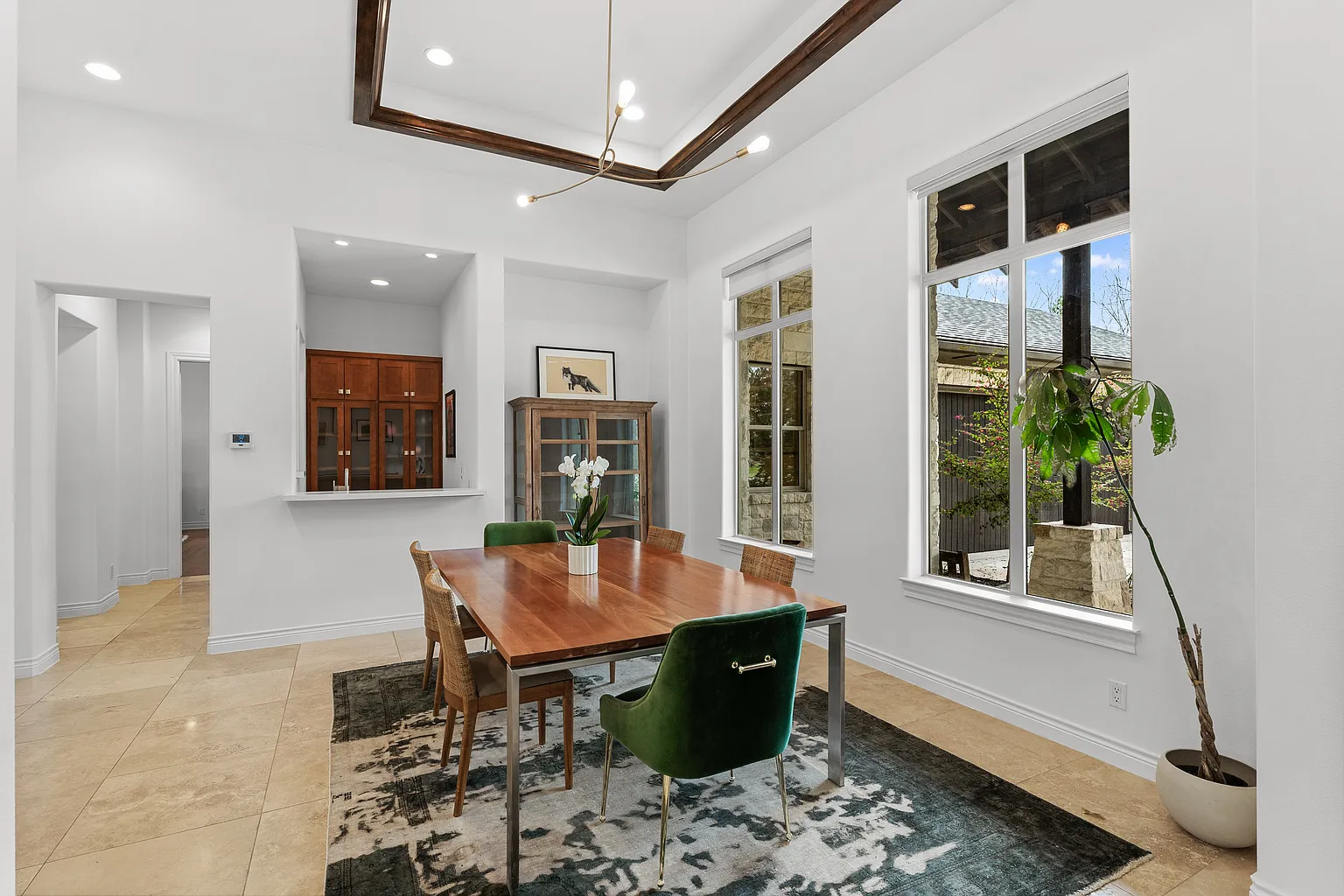 At the center, a long wood dining table sits over a patterned area rug, surrounded by a mix of woven side chairs and green upholstered host chairs. 