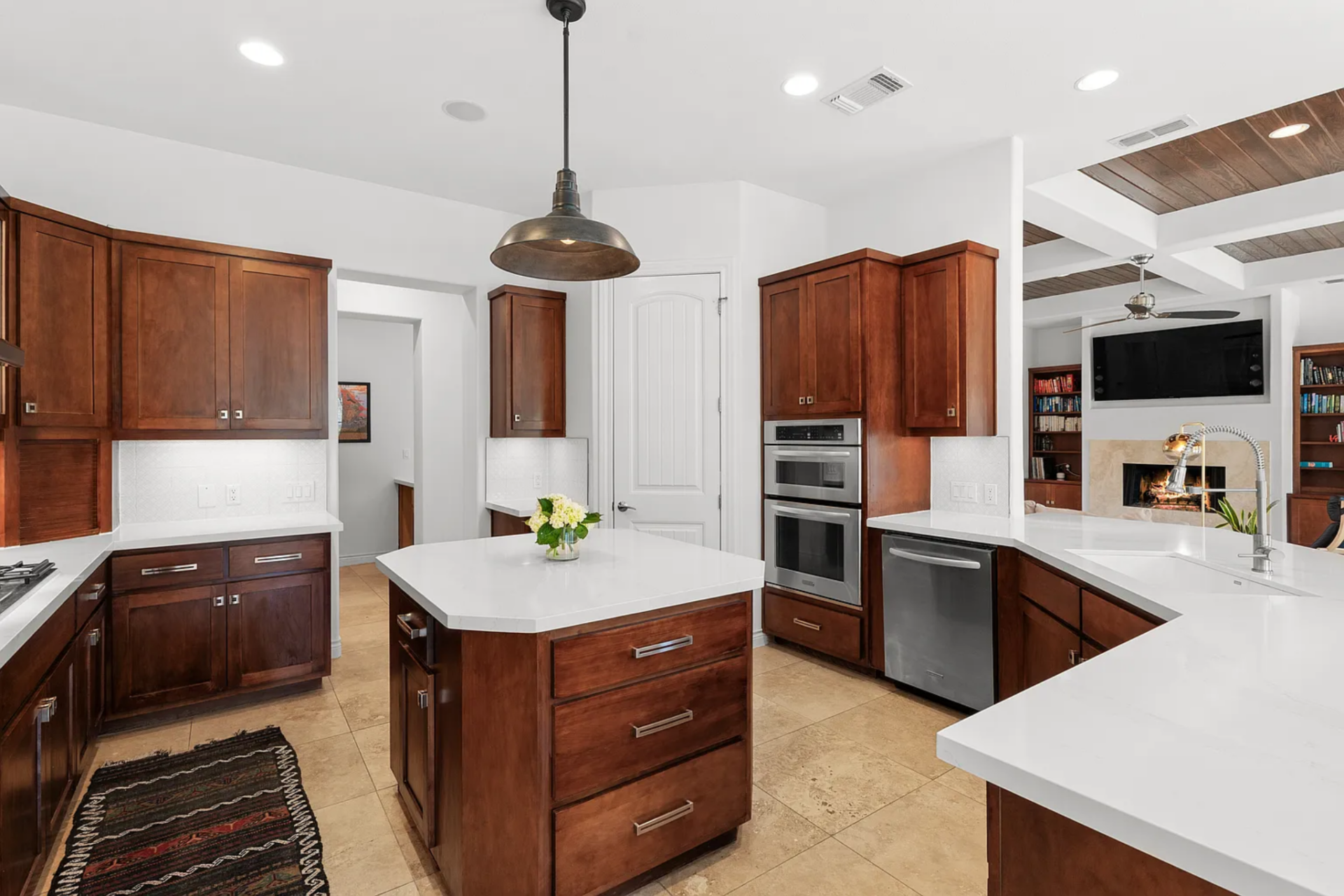 Just beyond the main living area, the kitchen has medium-toned wood cabinetry that wraps the room on multiple sides, paired with bright quartz counters that lighten the overall palette.