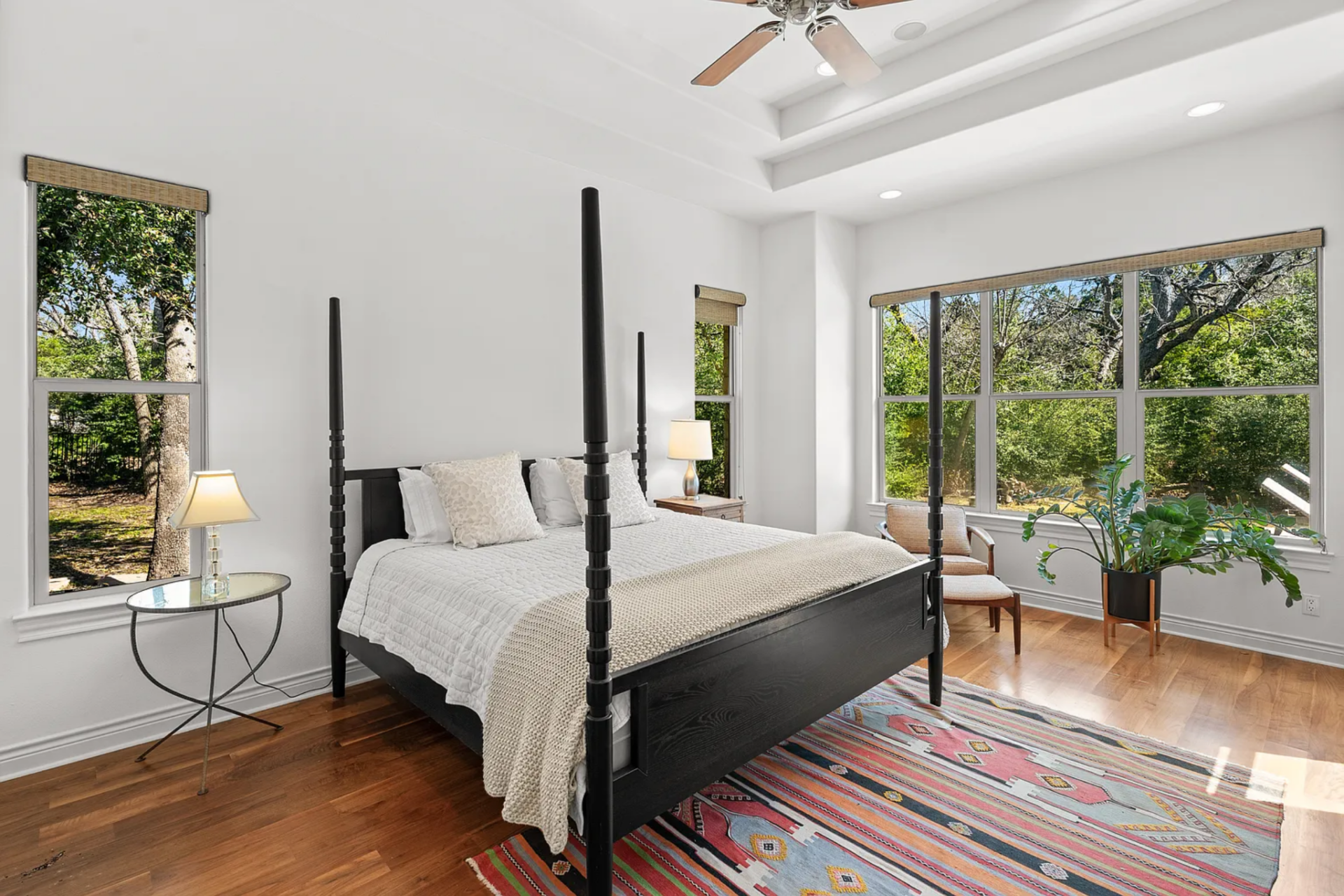 The bedroom centers around a four-poster bed positioned next to a wall of large windows that look out onto the surrounding trees. 