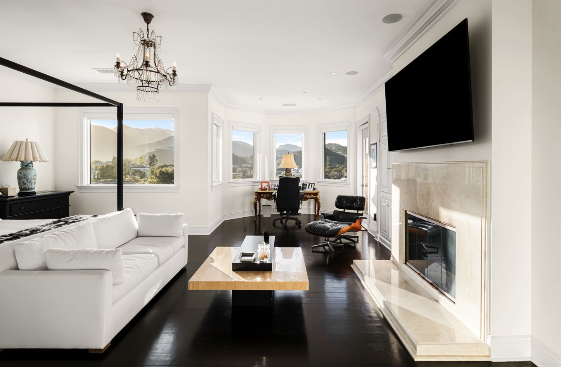 The layout opens further toward a secondary seating area and workspace, near the fireplace and a wall-mounted TV.