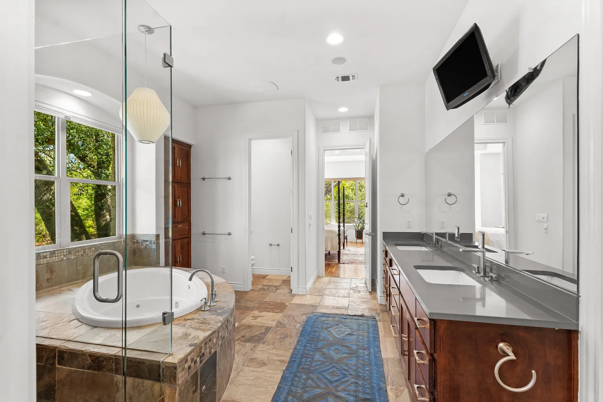 A long double vanity with wood cabinetry and a dark countertop runs along one wall, paired with a full-width mirror above. 