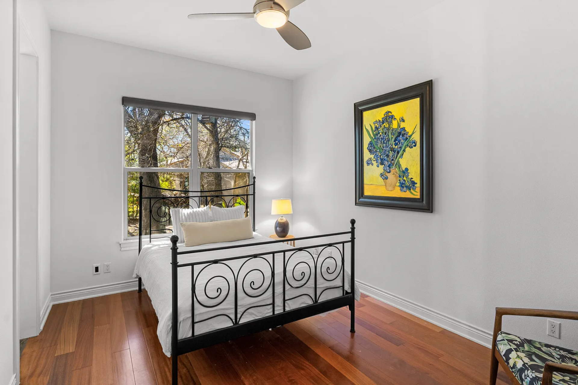 The first bedroom is arranged with a metal bed frame centered against the wall beneath a large window. 
