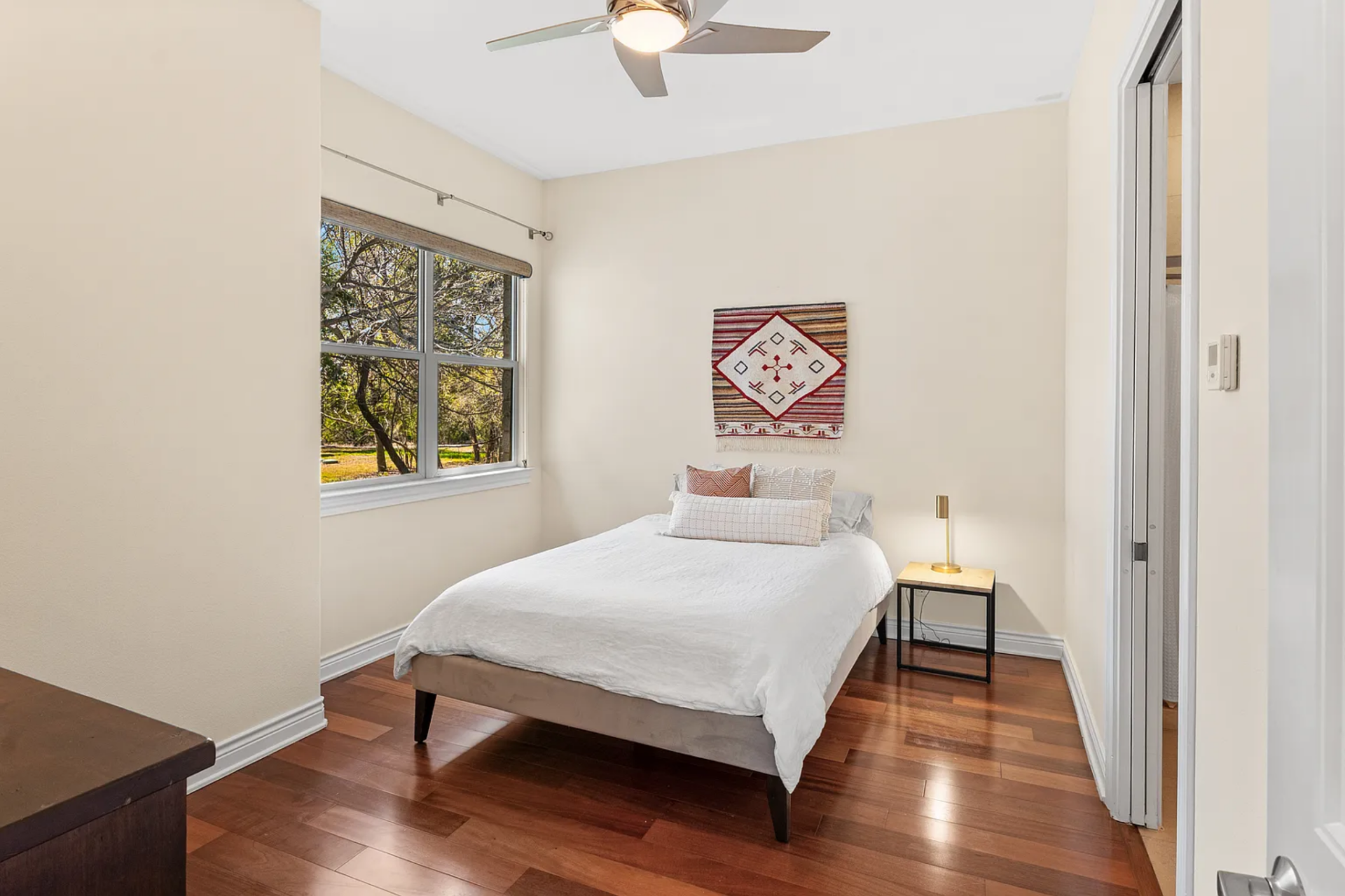 The second bedroom introduces a slightly warmer palette, with soft-toned walls and a low-profile upholstered bed positioned beneath a textile wall hanging. 