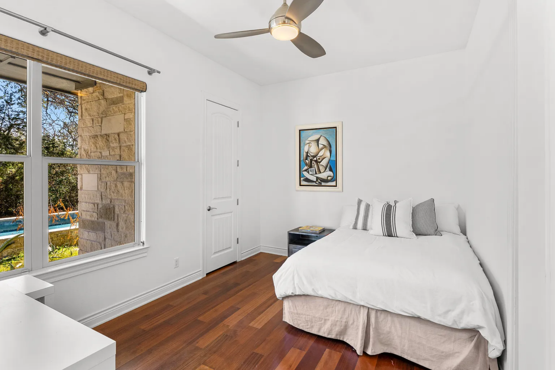 The third bedroom has a bed placed along one wall near a window that looks out toward the pool and exterior stonework. 