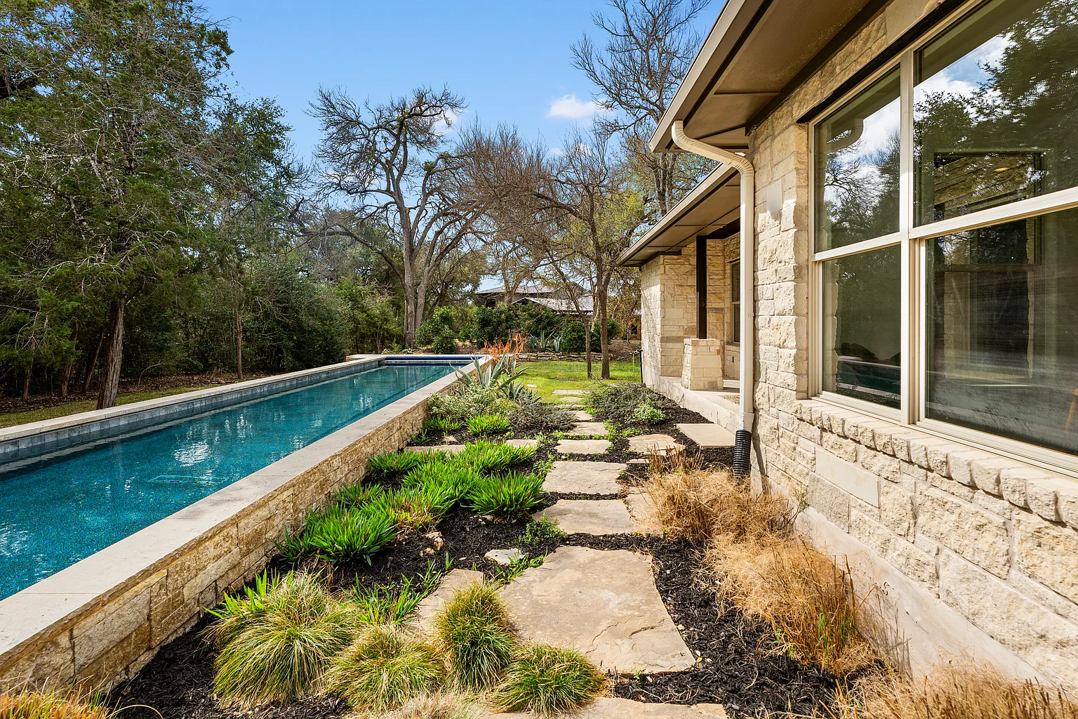 At the center of the outdoor space is a raised 80-foot lap pool, positioned alongside limestone terraces and open lawns.