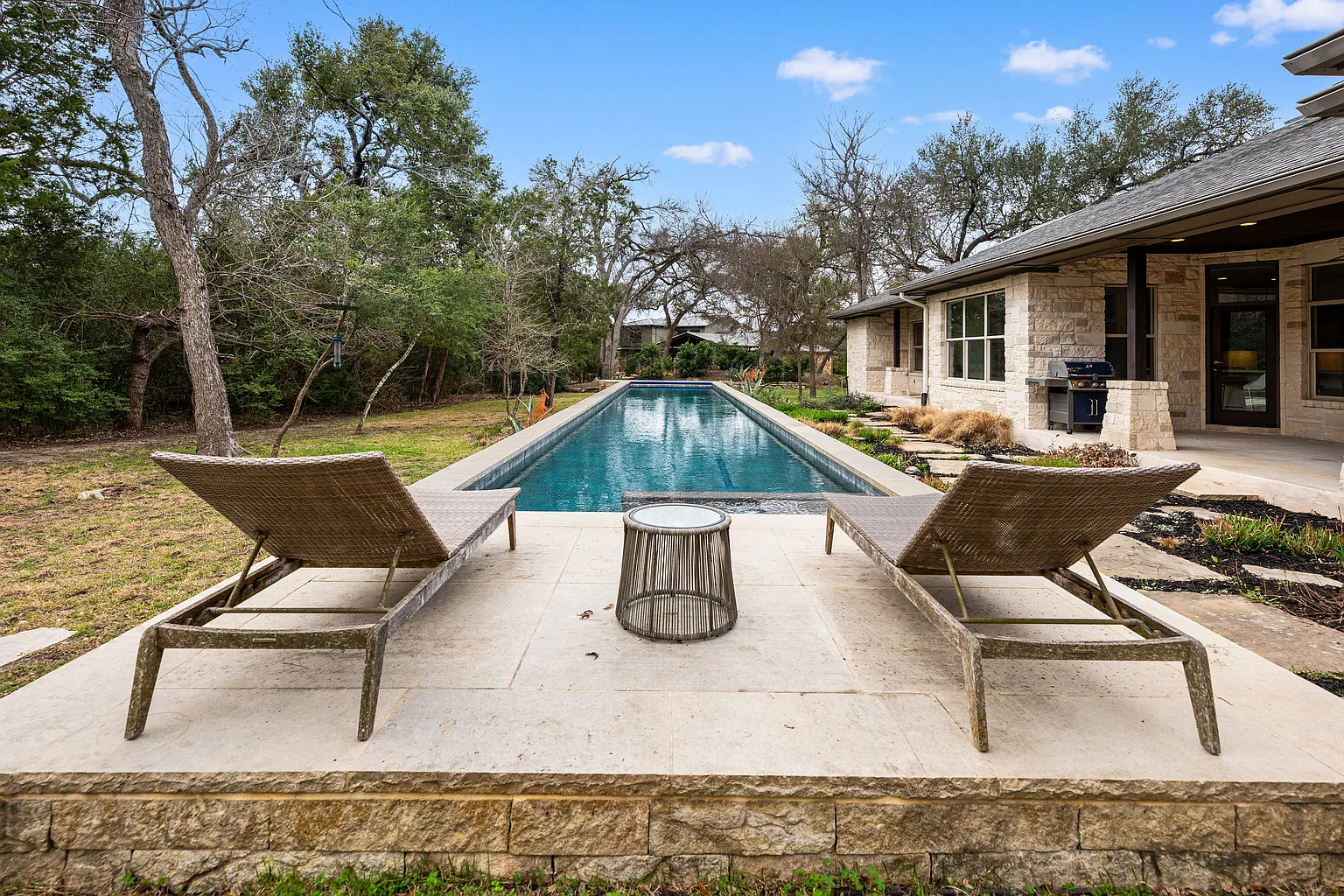 At the center of the outdoor space is a raised 80-foot lap pool, positioned alongside limestone terraces and open lawns.