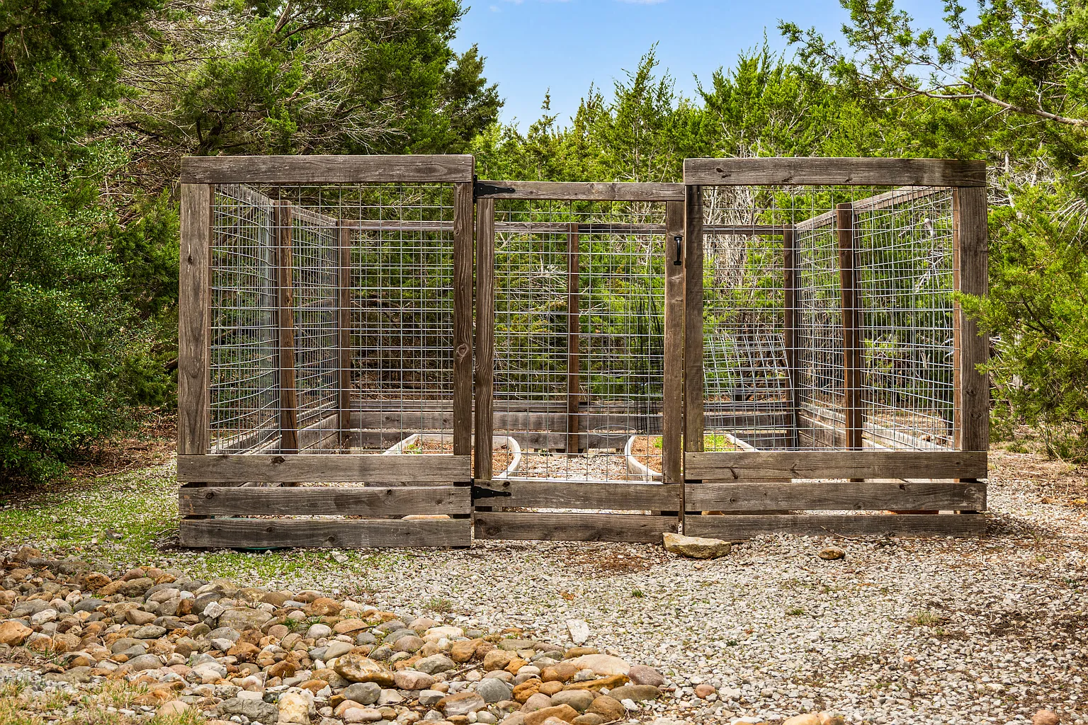 Near the main outdoor areas, the herb garden is set up as a compact enclosed space with a simple wood-and-wire fence that protects the planting beds without interrupting the natural look of the landscape. 