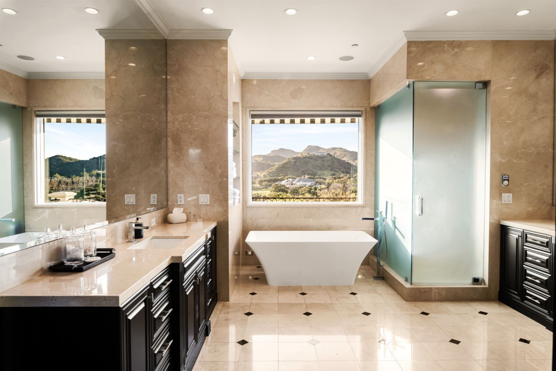 The first bathroom is finished in warm stone, with a freestanding tub placed directly beneath a window that looks out toward the hills. 