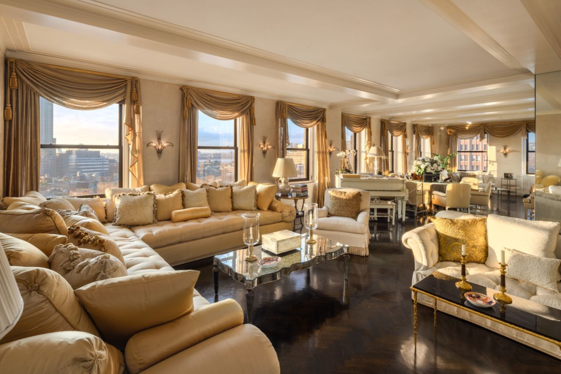 Dark glossy floors run wall to wall beneath a series of tall windows, while the room is wrapped in soft gold tones, layered drapery, and decorative sconces that give the entire space a consistent, highly styled look.