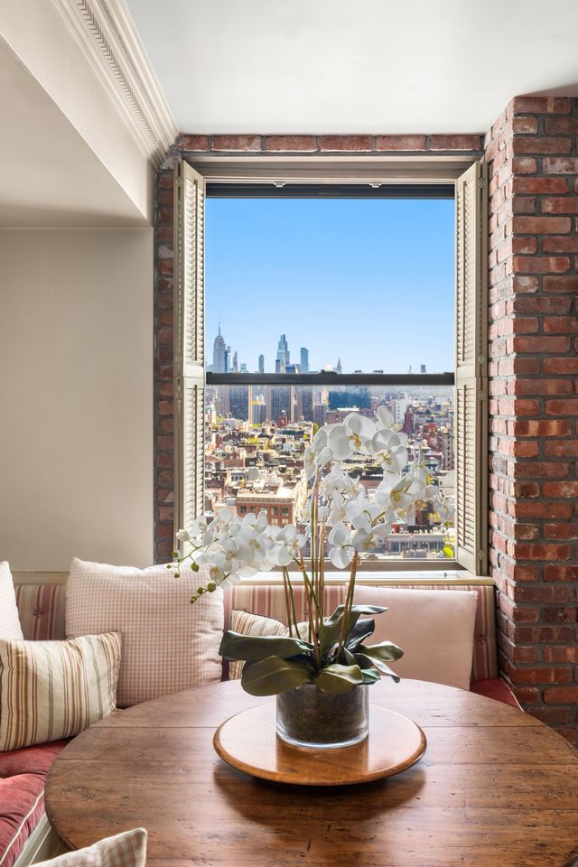 A built-in banquette wraps around a round wood table, creating a compact spot for coffee or casual meals, while exposed brick around the window adds a more grounded note to the otherwise polished interior.