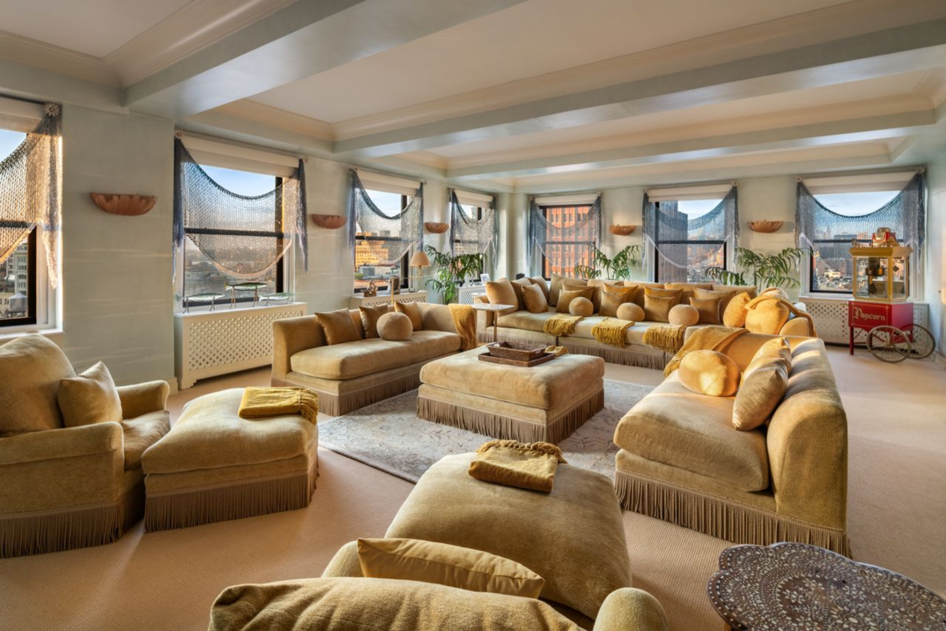 Here, the palette shifts fully into warm neutrals, with fringed sofas, oversized ottomans, and low lounge seating arranged around a central rug made for movie nights.