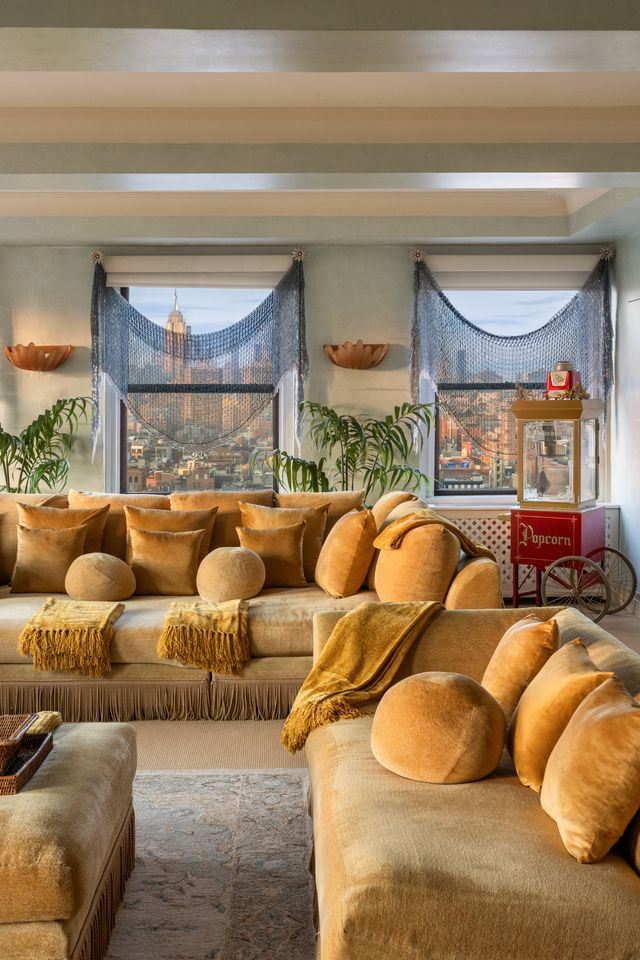 The room still follows the penthouse’s theatrical design style, but in a more relaxed way, with a coffered ceiling framing a row of city-facing windows dressed in draped, net-like curtains. 