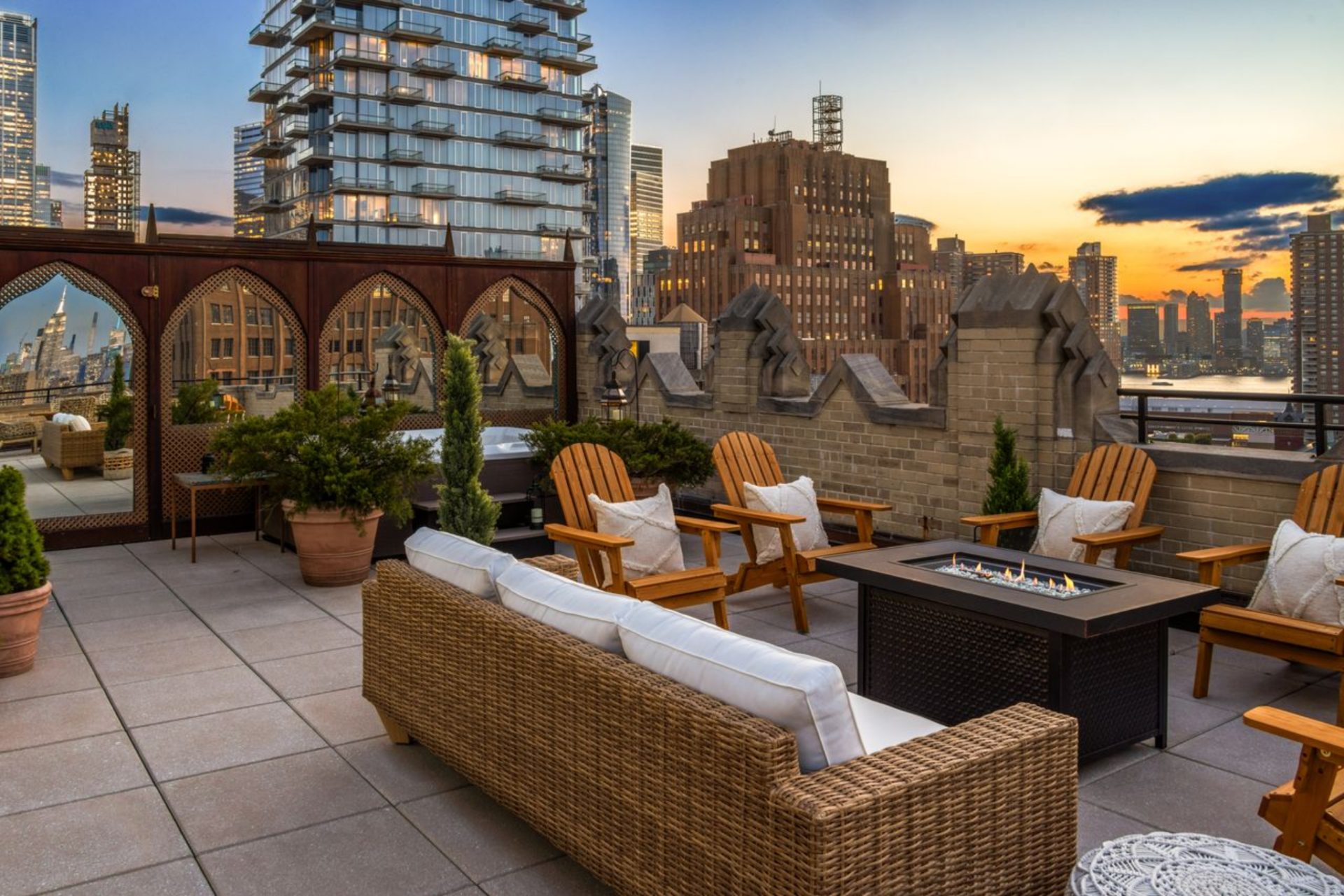 One section is arranged as a lounge, with Adirondack chairs and a wicker sofa gathered around a linear fire feature, creating a clear spot for evening entertaining against the skyline. 