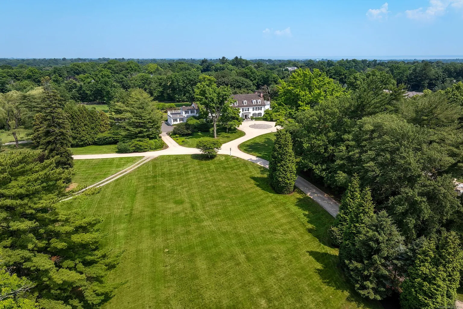 The property includes rolling lawns, a one-acre pond, and a network of walking paths that move through gardens and wooded areas around the main house.