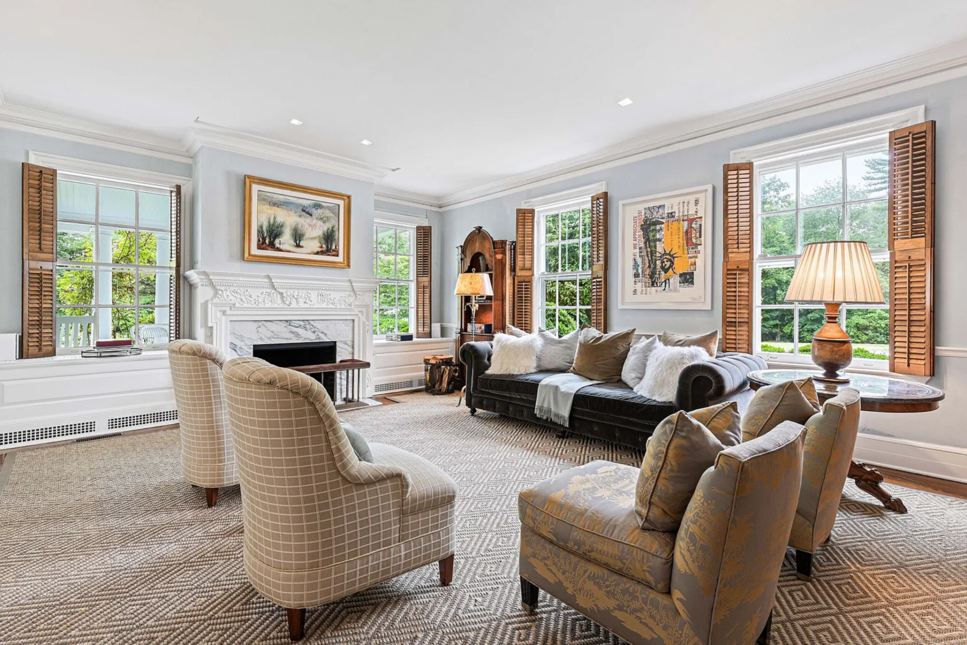 Off the central entrance hall, the first formal living room continues the home’s traditional tone with a carved white mantel with a marble firebox surround, which anchors the far wall between two tall windows.