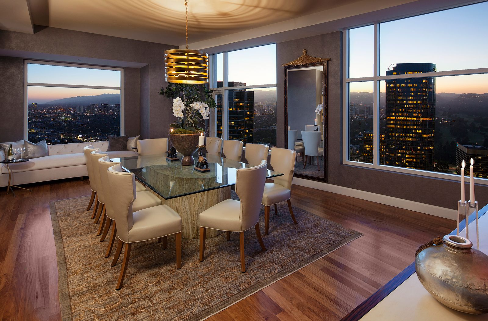 The formal dining room features a glass-top table with a large stone base surrounded by upholstered dining chairs that keep the setup clean and tailored without feeling too rigid.