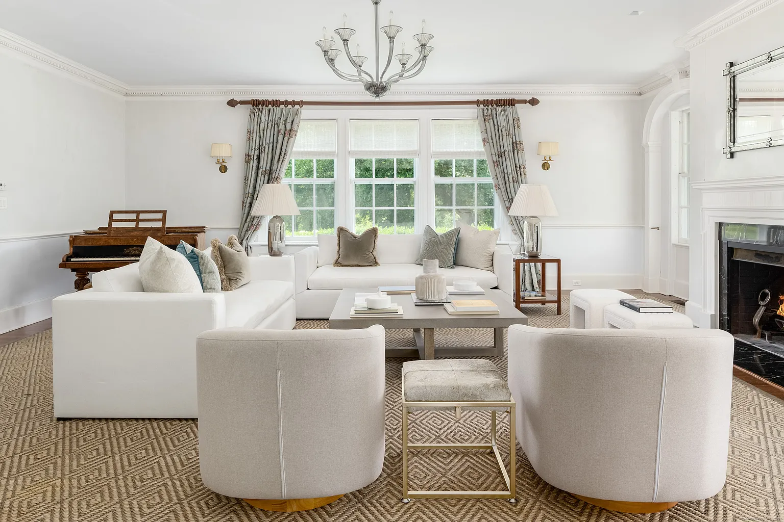 The seating is arranged in a tighter layout, with two white sofas facing each other across a low square coffee table, and a pair of rounded swivel chairs, while a piano is tucked off to the side.