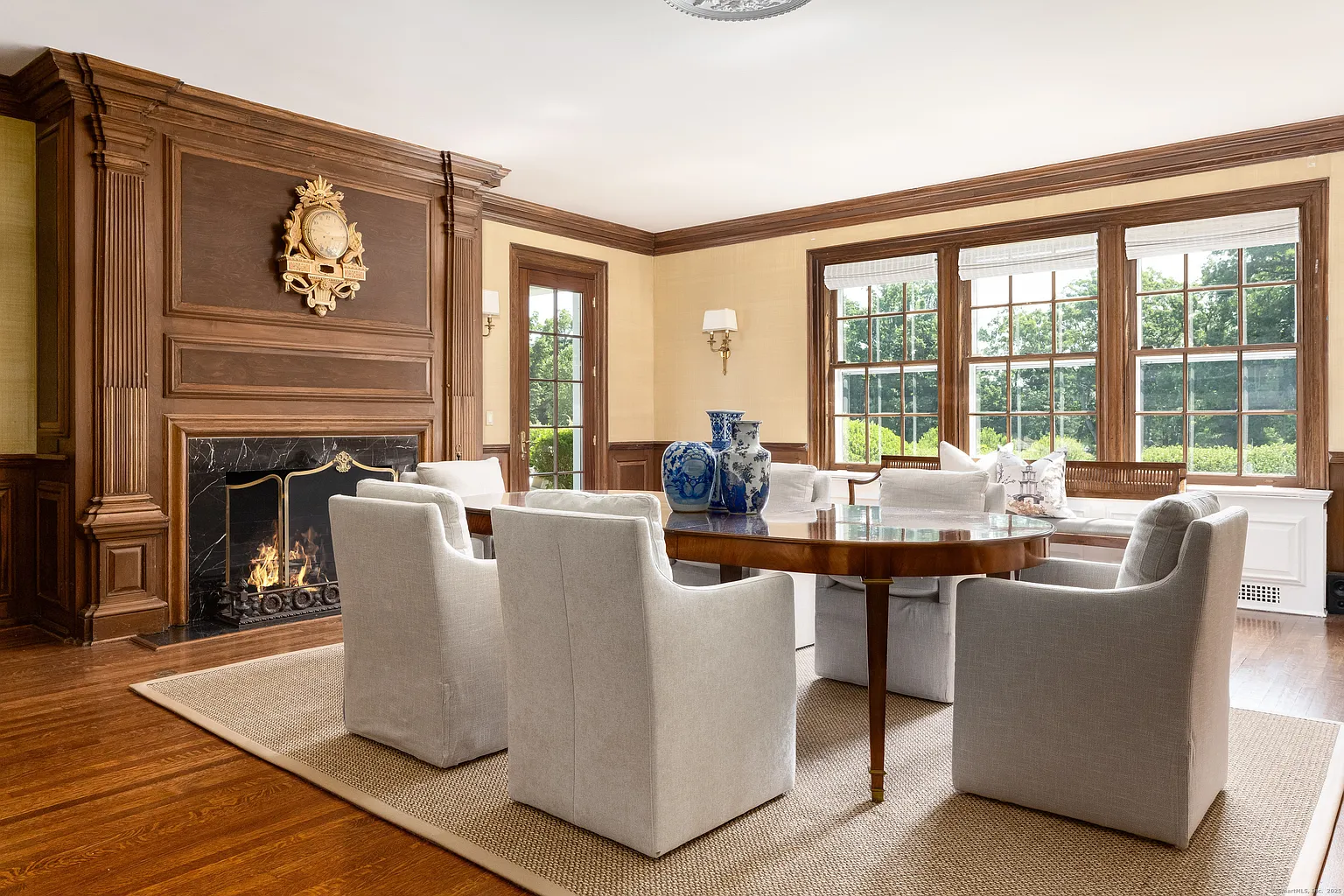 Down the hall, the formal dining room features a curved dining table framed by dark wood paneling and a black marble fireplace wall.