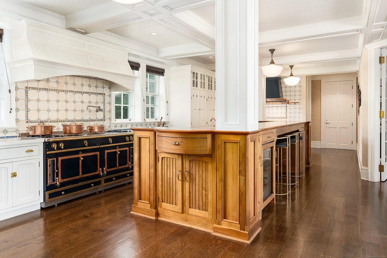  Around them both, the cabinetry stays crisp and orderly, while the island adds warmth through its wood finish, integrated wine storage, and bar seating.
