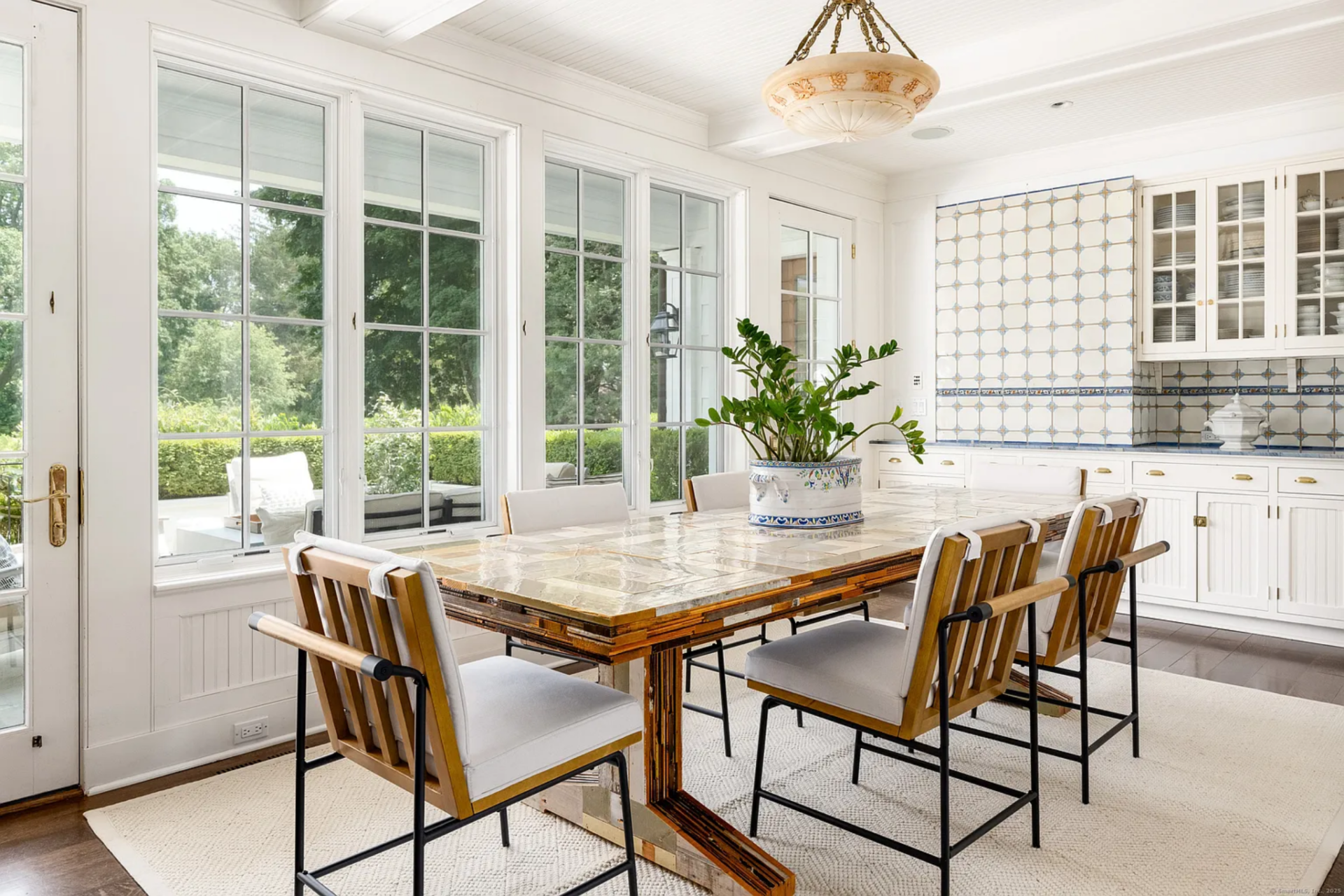Alongside the second La Cornue range, the breakfast area is a bright space with a large table sitting in front of a wall of windows and a glass door, bringing in garden views and direct access outside.