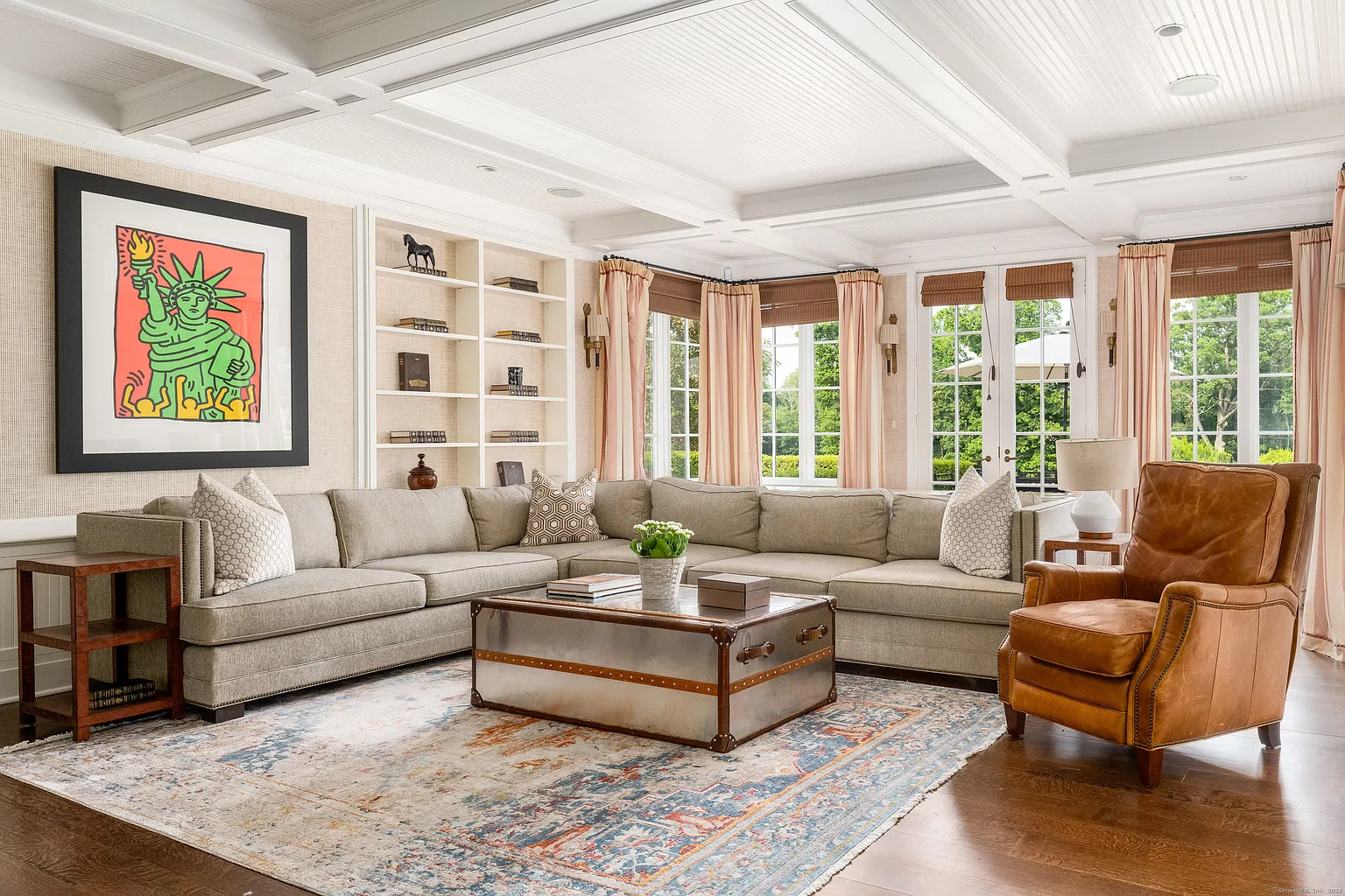 Moving out of the kitchen, the layout opens into the family room, where a large sectional sits beneath a coffered ceiling, positioned to face inward around a trunk-style coffee table.