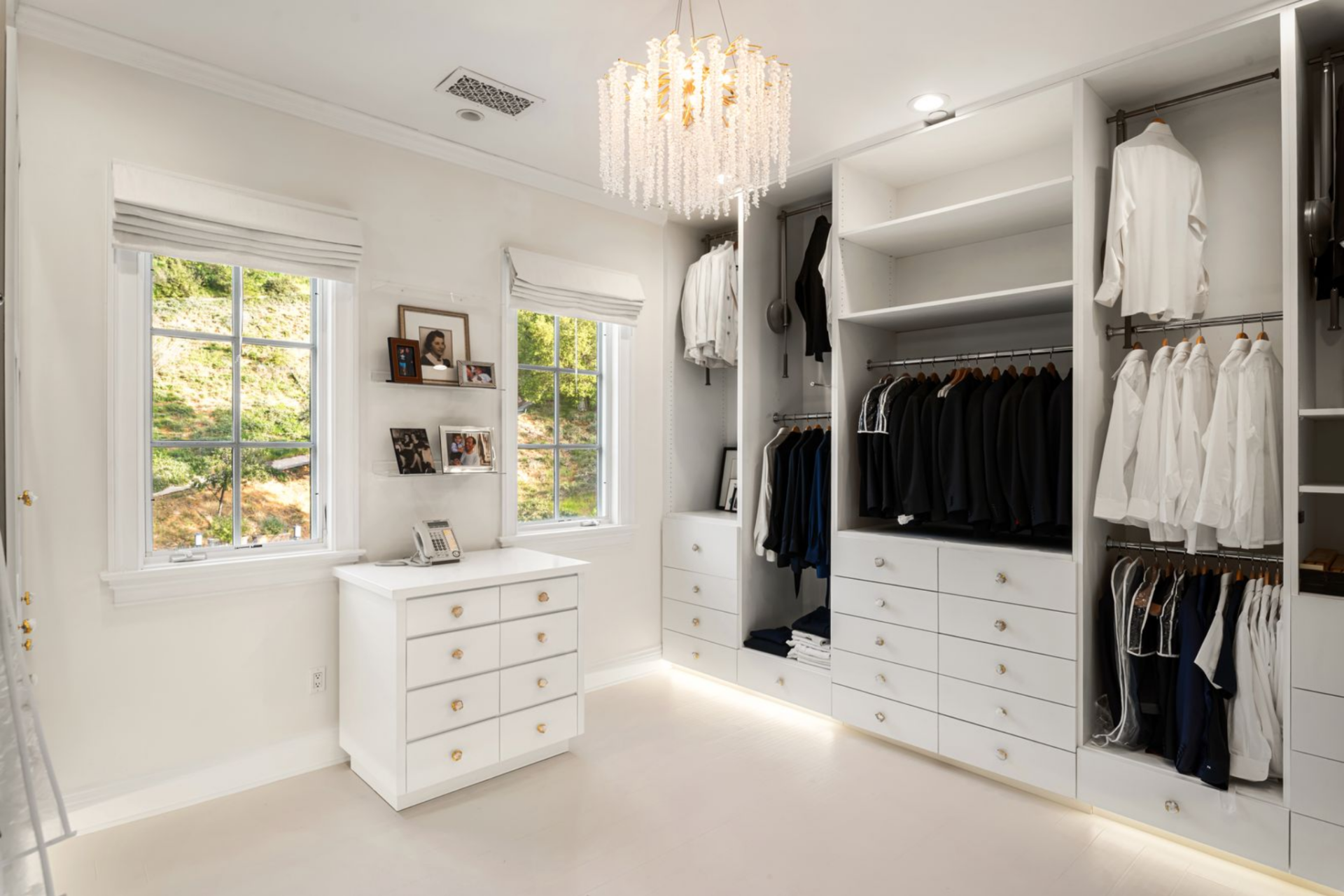 The second closet opens up into a brighter dressing room, with white built-in cabinetry arranged along the walls and underlit at the base. 