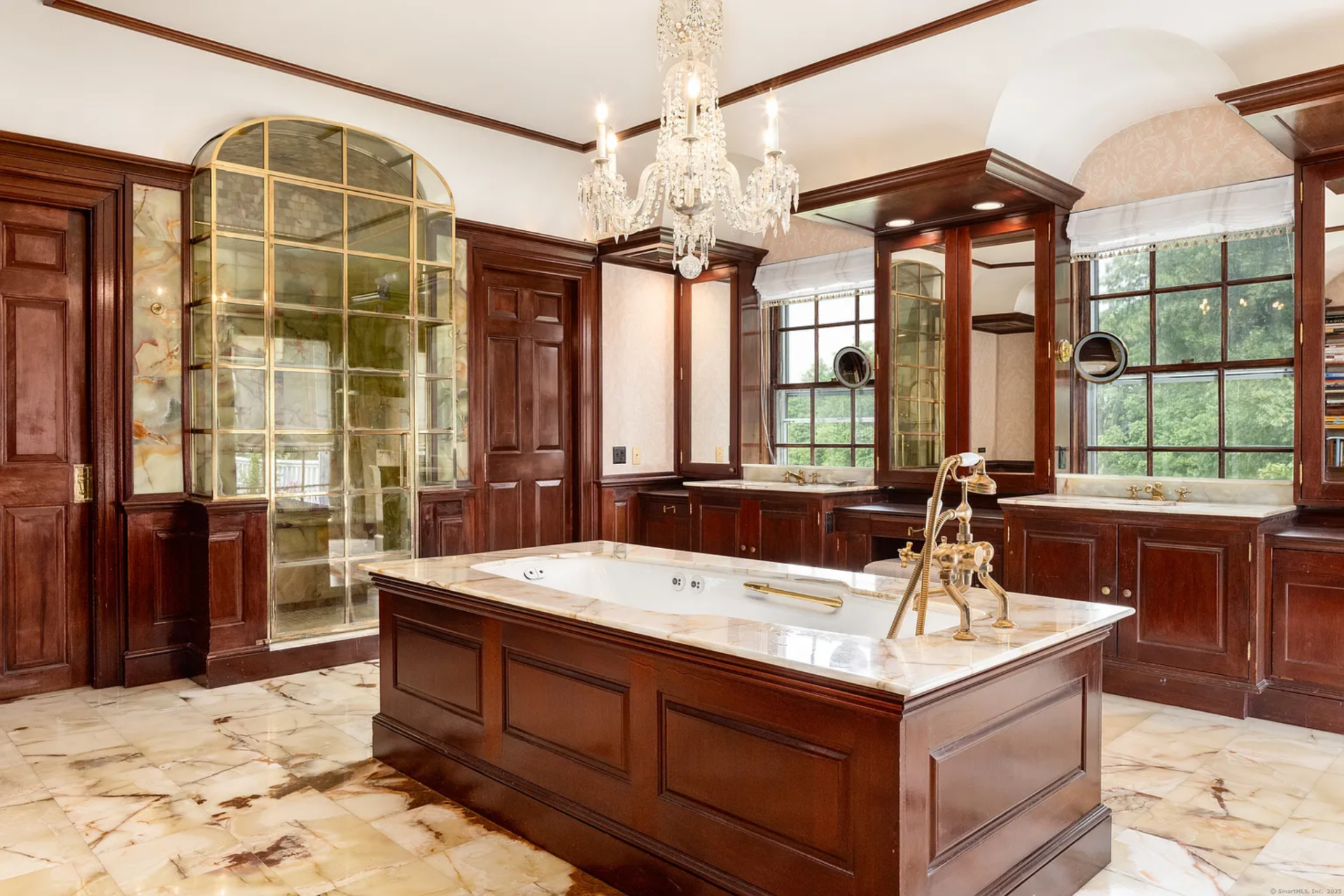 The suite's bathroom continues the more traditional detailing with dark wood cabinetry, marble flooring, and a crystal chandelier suspended over a large soaking tub set into the center of the room. 