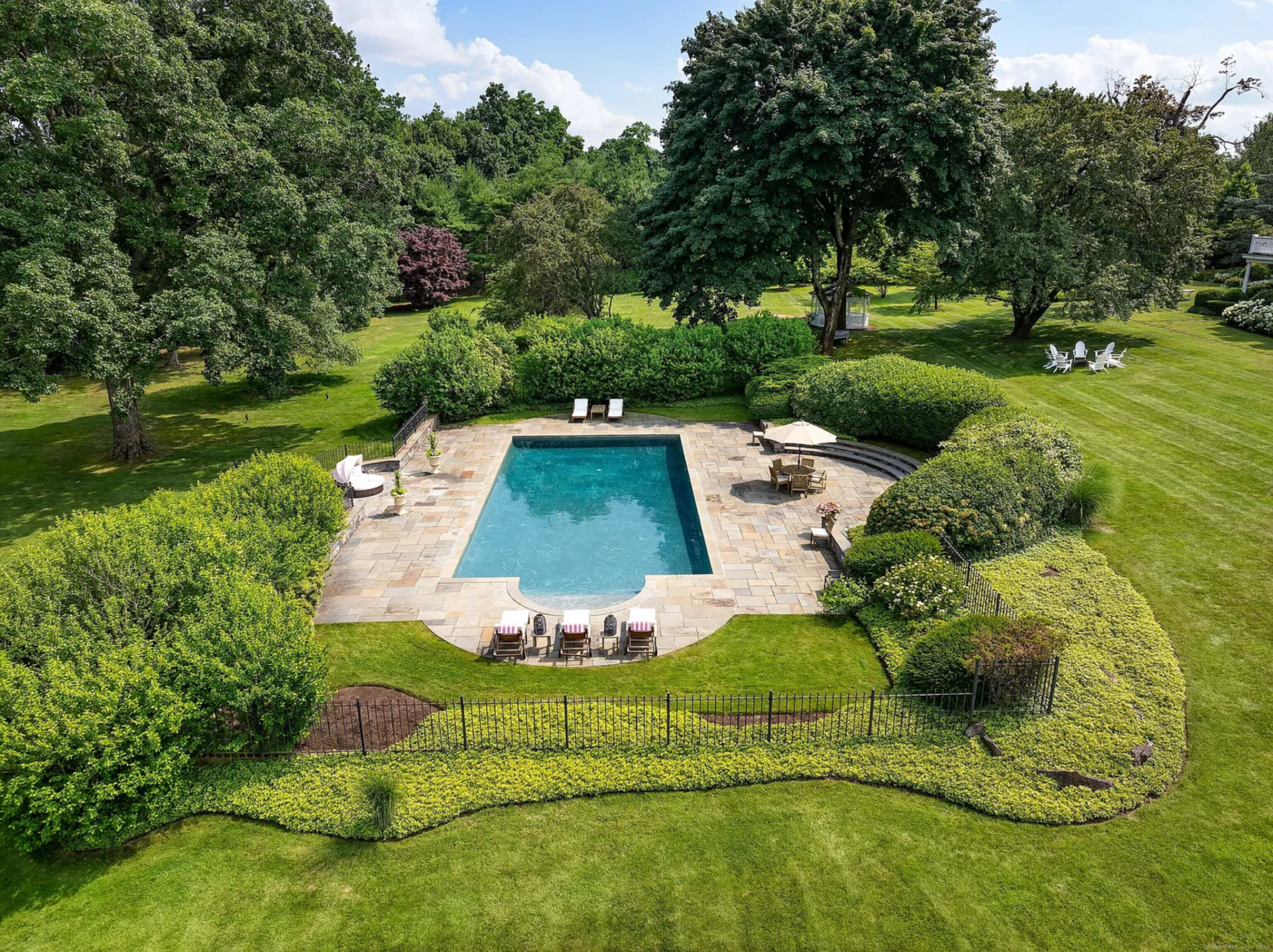 The saltwater pool sits in its own hedged enclosure, framed by a broad stone surround with space for loungers, umbrella seating, and curved steps built into one side.