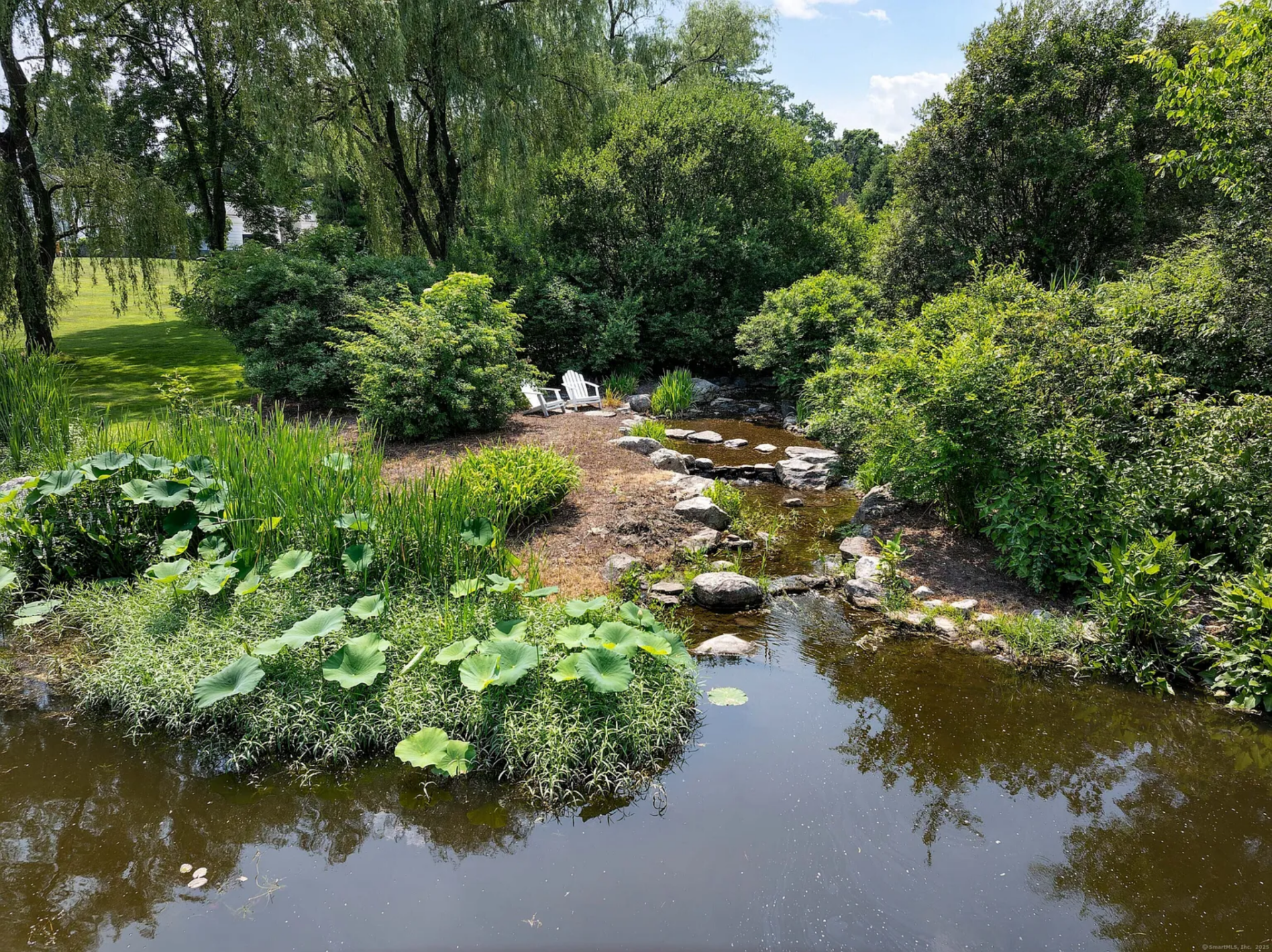 Elsewhere on the property, the koi pond introduces a more natural setting, with water moving around planted edges, stones, and a small seating area tucked into the greenery.