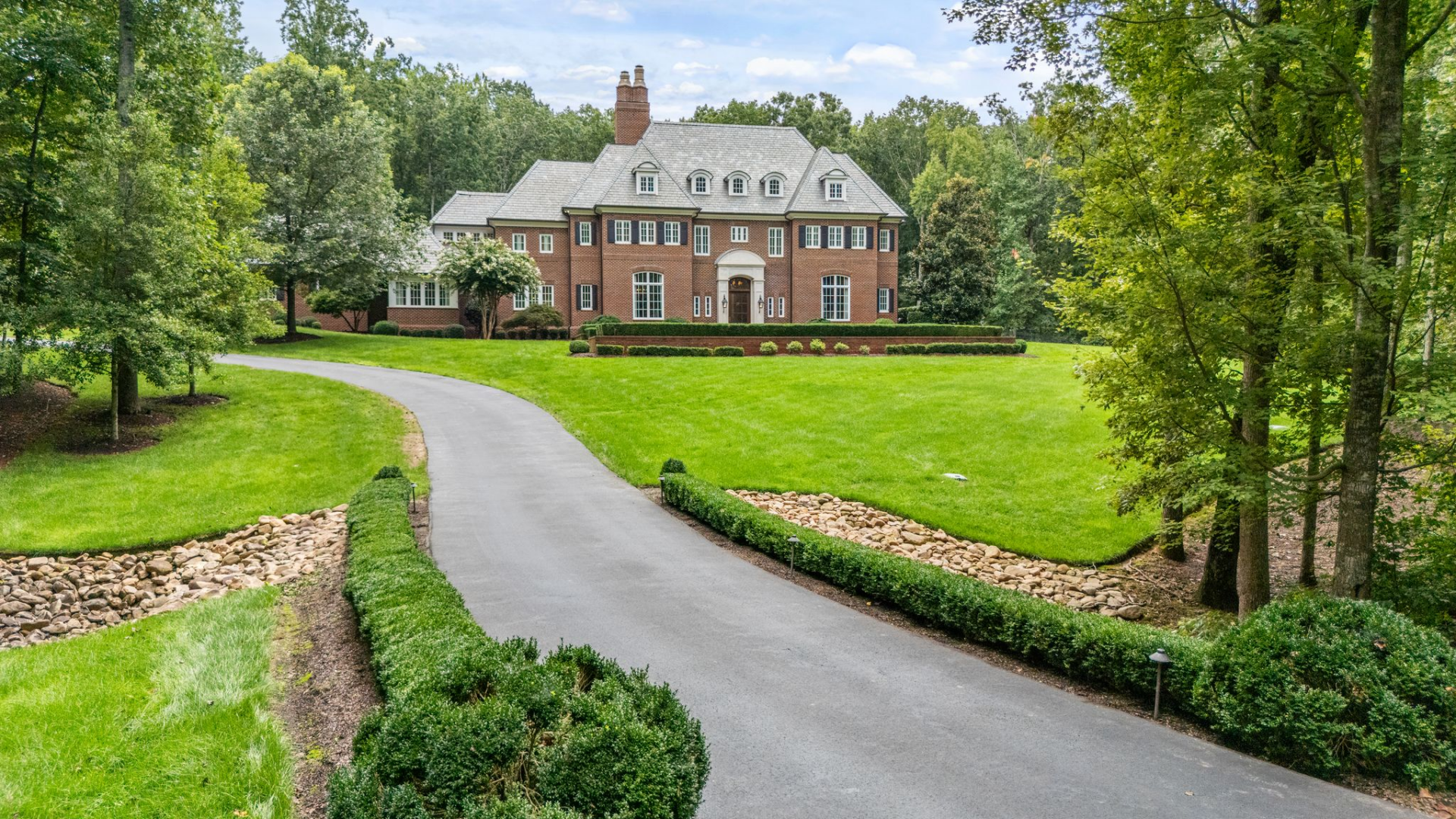 As the drive straightens, the home's symmetrical red brick exterior is set slightly elevated above the lawn. 