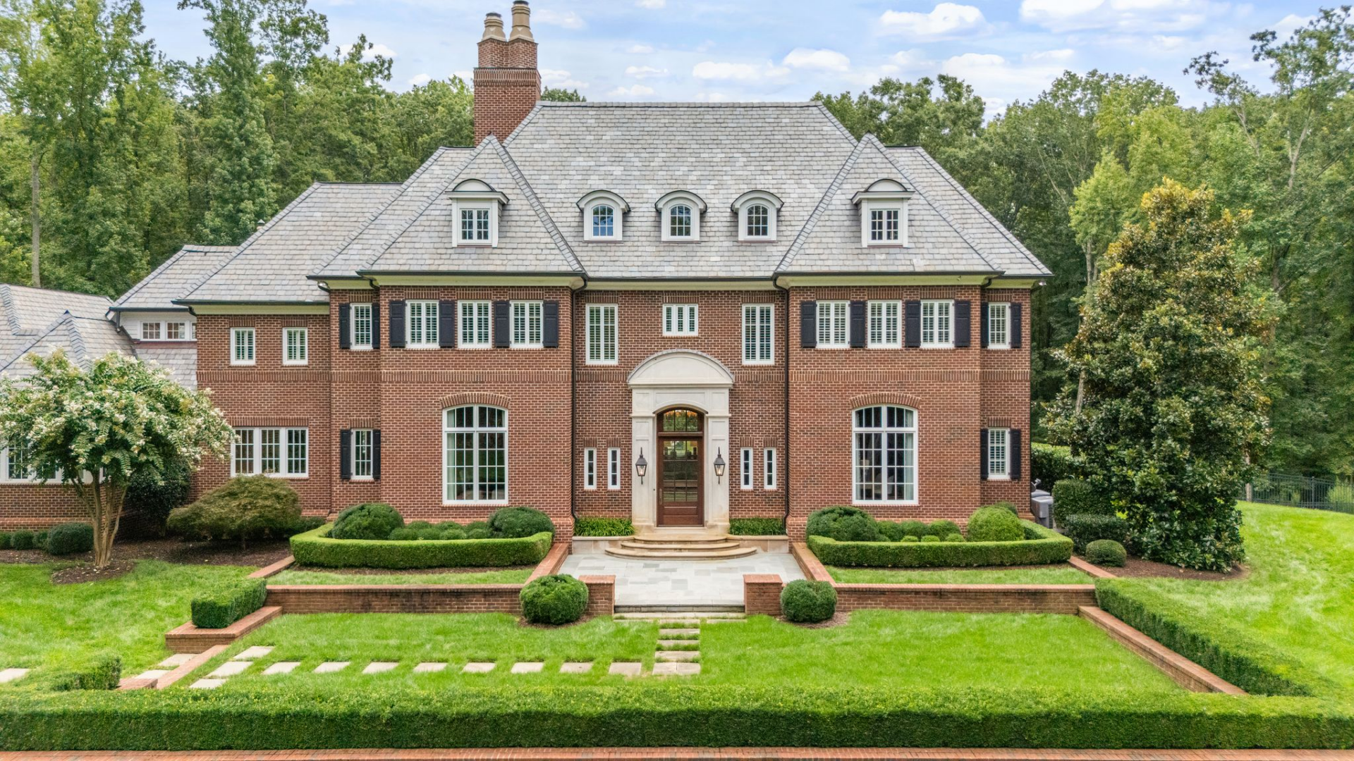 A short set of stone steps leads up to the front door, which sits beneath a classic arched surround, framed by lantern-style lighting and evenly spaced windows.