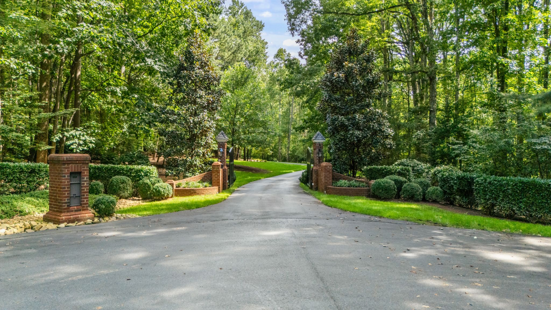 Driving through the gated entrance, the property opens with a long, curving asphalt driveway that gradually reveals the home as you move forward. 