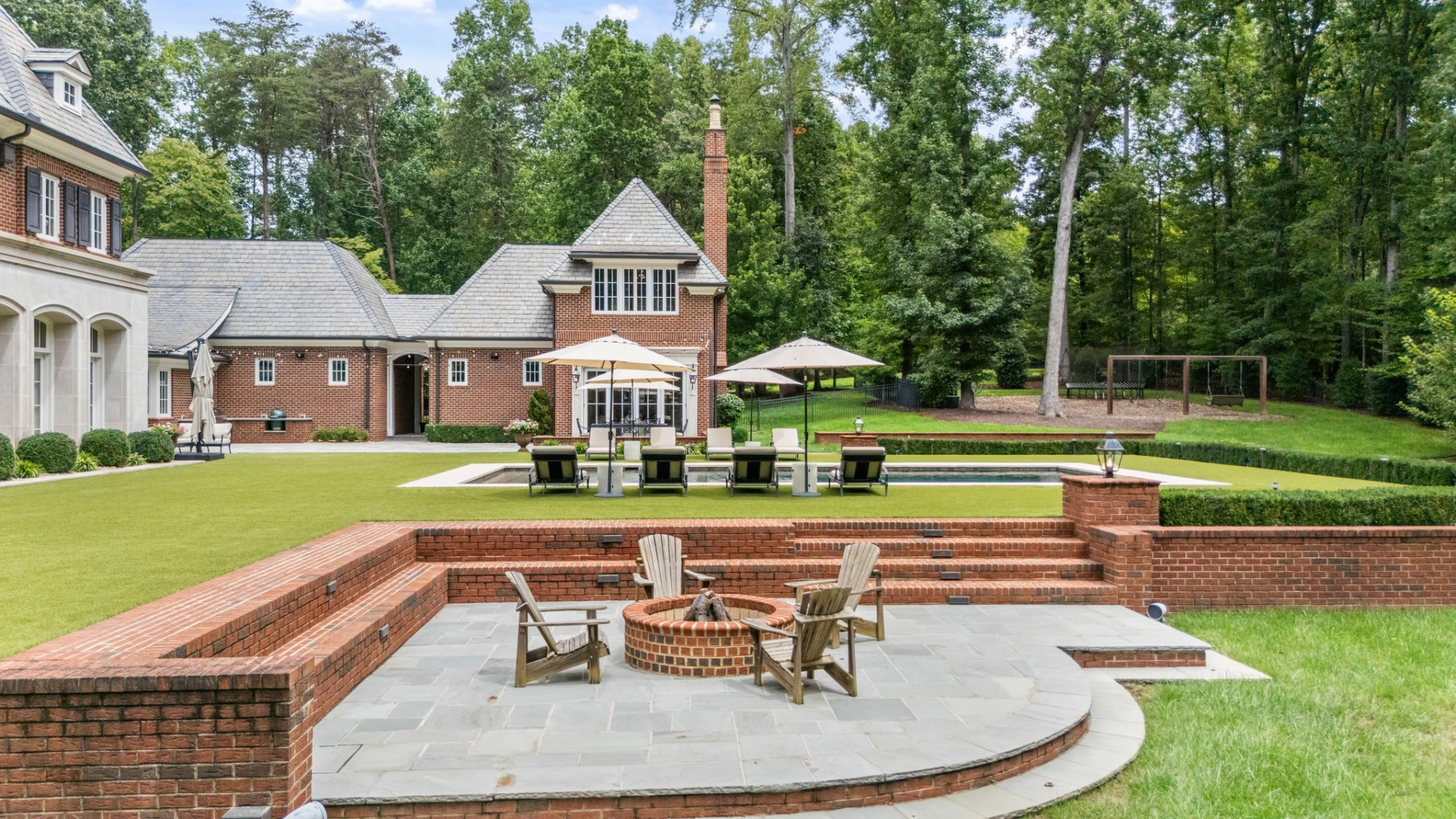 Just below the pool terrace, a set of brick steps leads down to a circular firepit lounge built into a paved patio. 