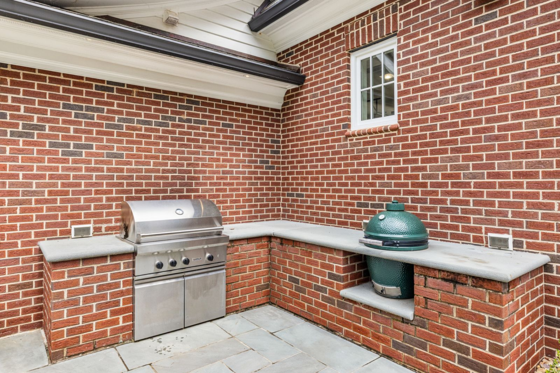 Next to the main patio, the outdoor kitchen is built into a brick alcove with a built-in grill and a separate ceramic smoker set into stone countertops.