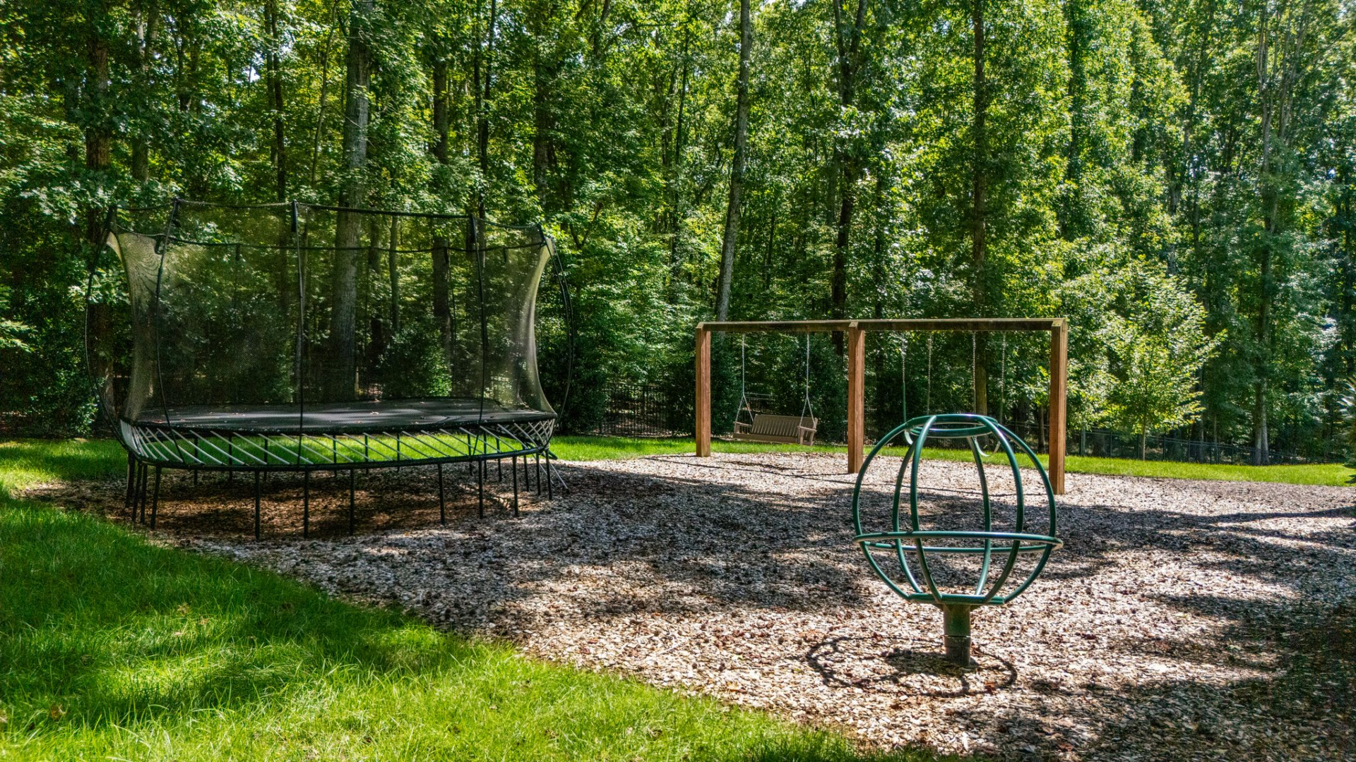 Off to the side, the property transitions into a more casual park-like setting, where a swing set, trampoline, and open mulch-covered play area sit beneath mature trees.