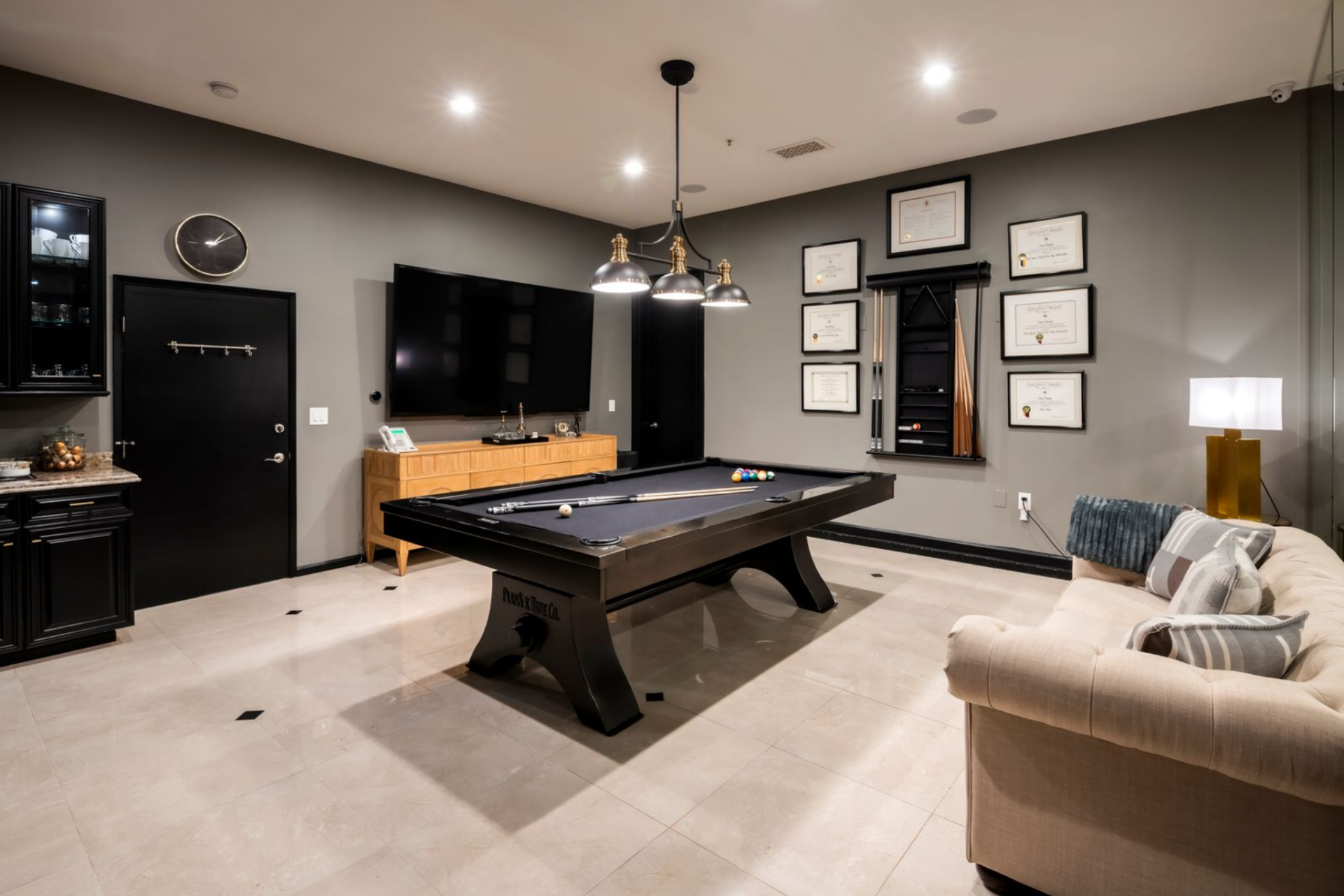 Surrounding walls are finished in a darker tone and lined with framed certificates and a mounted cue rack, giving the space a more tailored, lounge-like feel.