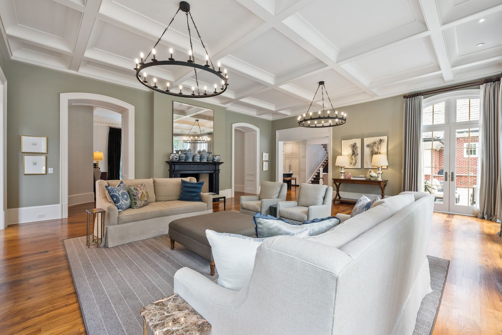 On one side, a sitting area made up of sofas, armchairs, and an upholstered ottoman is arranged near a dark fireplace mantel topped with blue-and-white ceramics and a tall mirror.