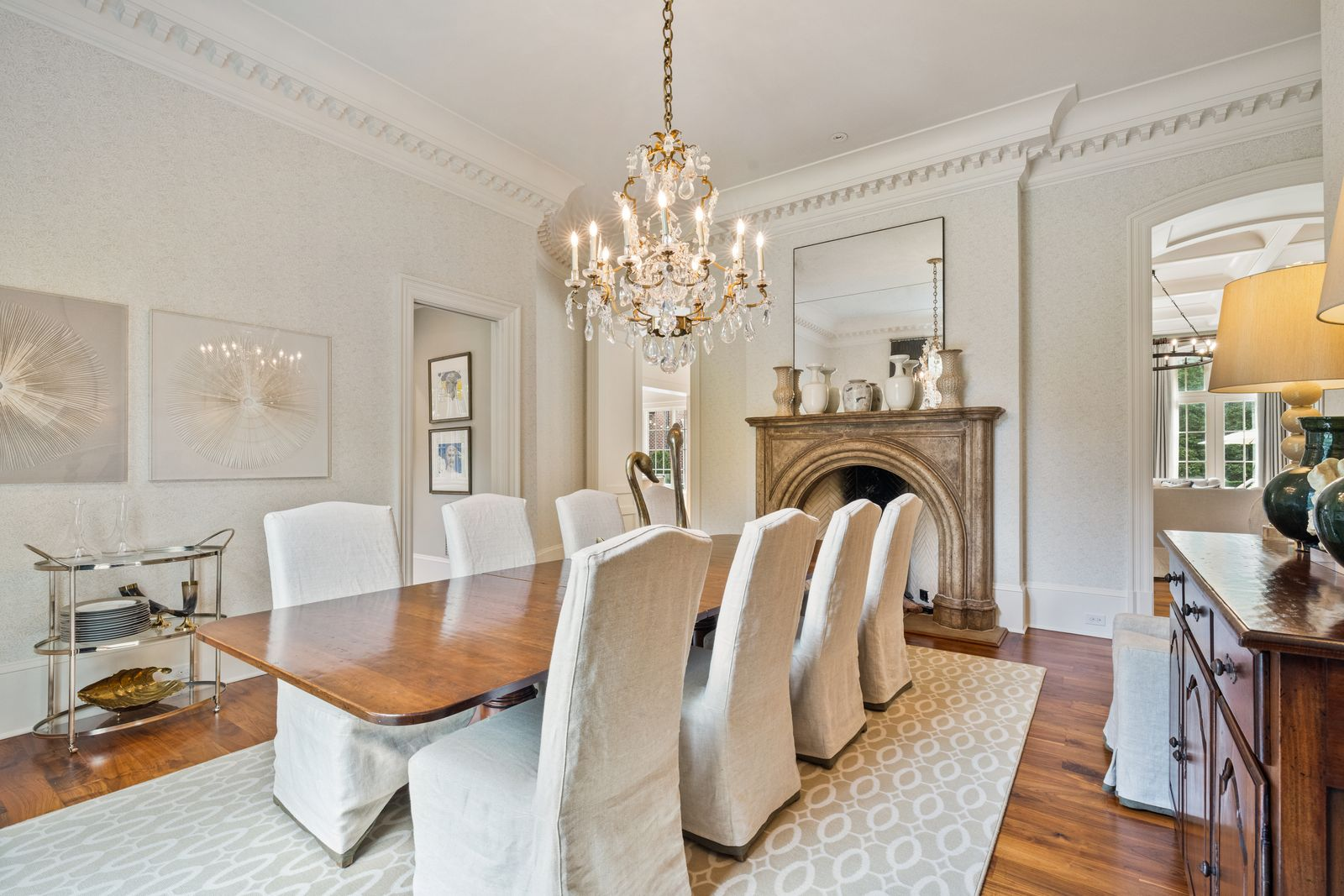 The space is centered around a long wood table surrounded by slipcovered chairs, with a crystal chandelier hanging above.