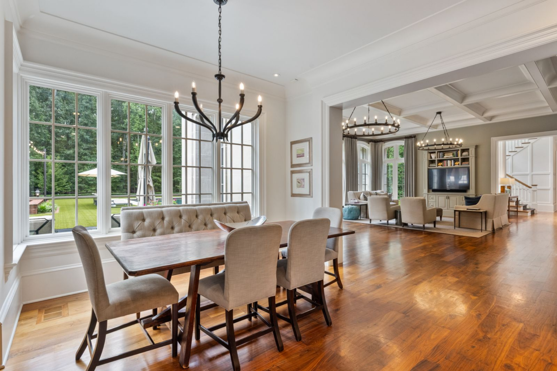 On the way to the kitchen, the home shifts into a more casual dining area made up of a rectangular wood table with upholstered dining chairs on three sides and a tufted bench tucked along the window line.