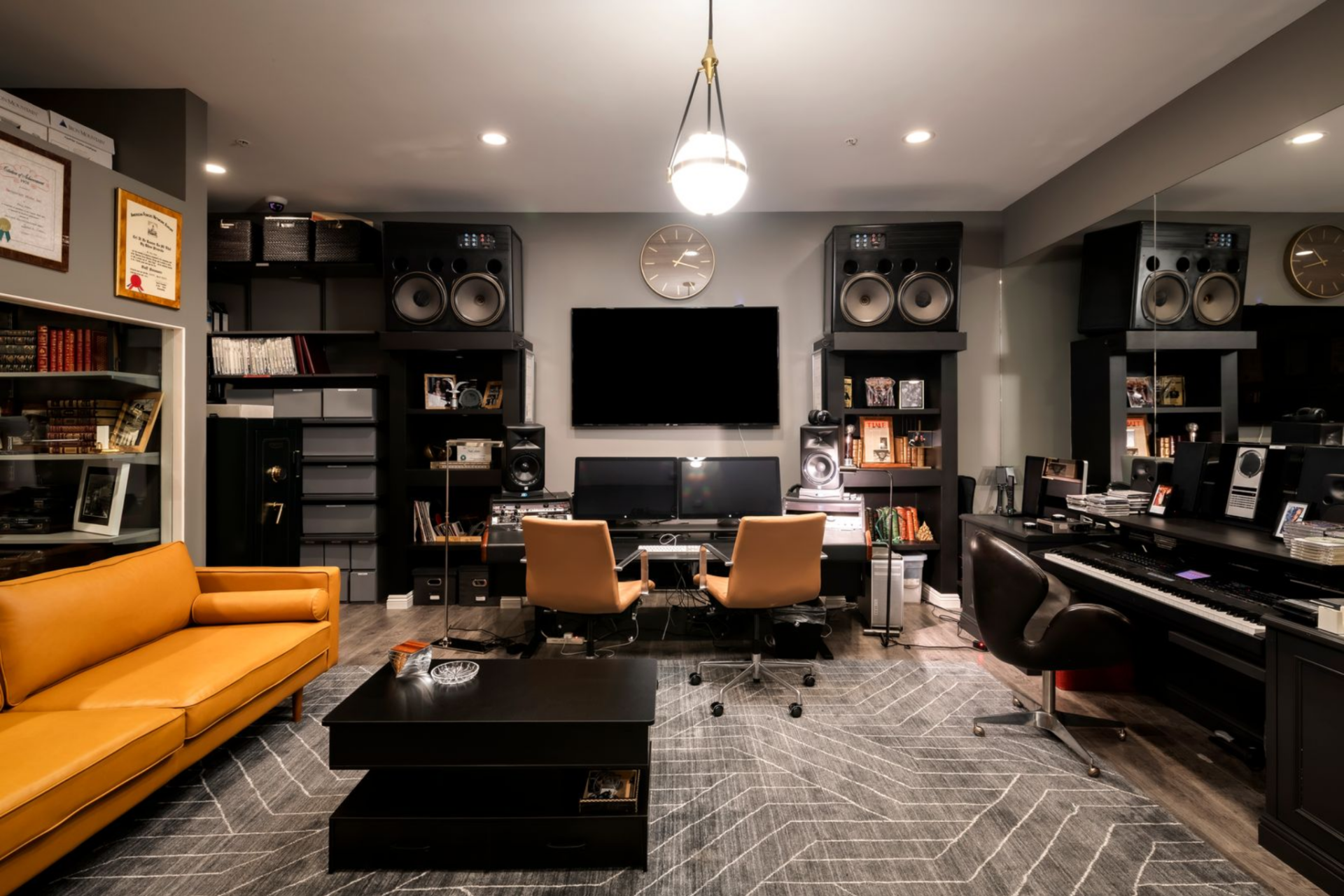 The main control room is anchored by a central production desk with dual monitors, framed by large speakers and built-in shelving filled with records, books, and equipment. 