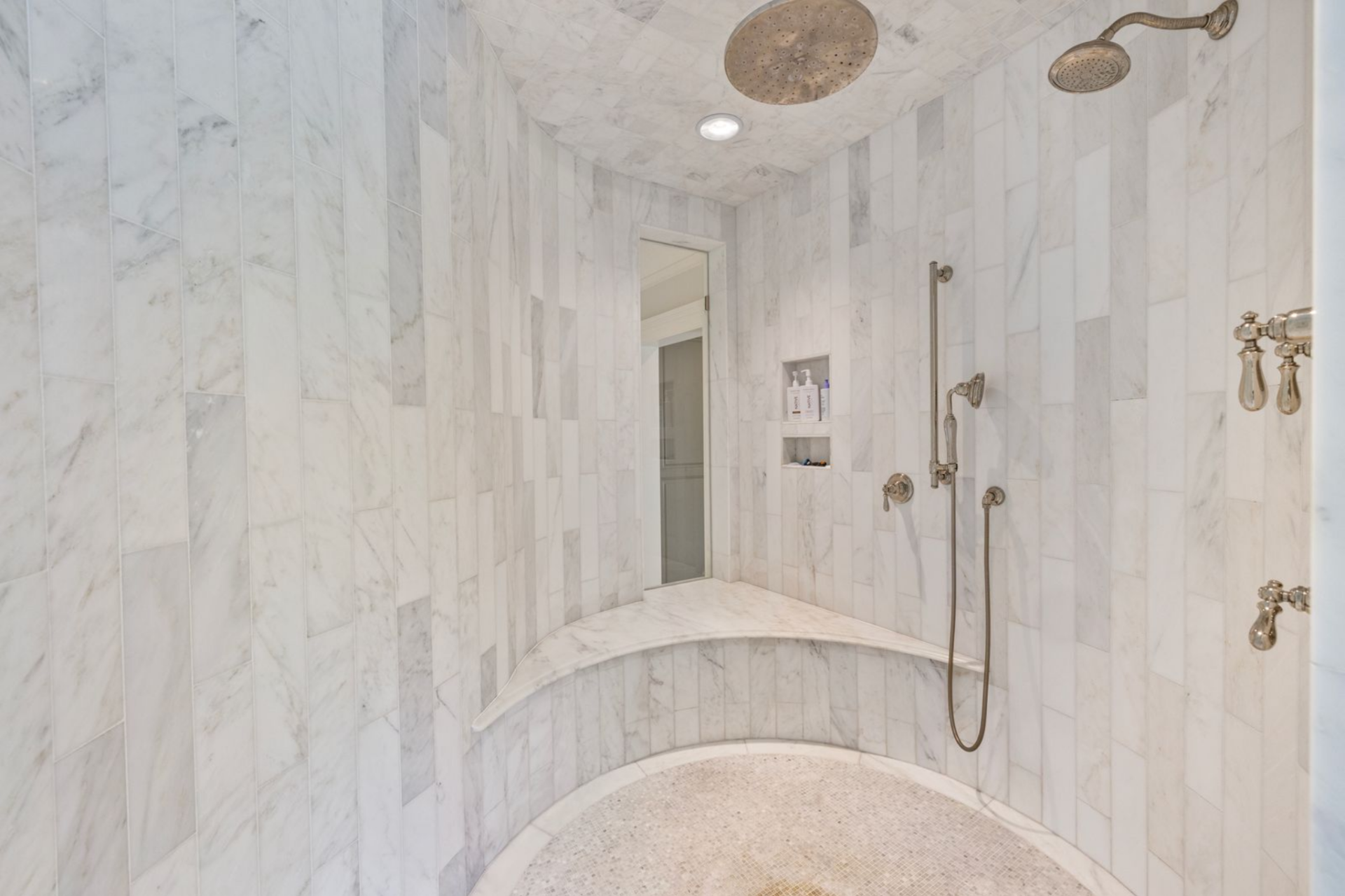 Across from those, the shower is built as a fully enclosed marble room with curved bench seating and overhead fixtures, reinforcing the bathroom’s scale and giving it a more custom, spa-style layout.