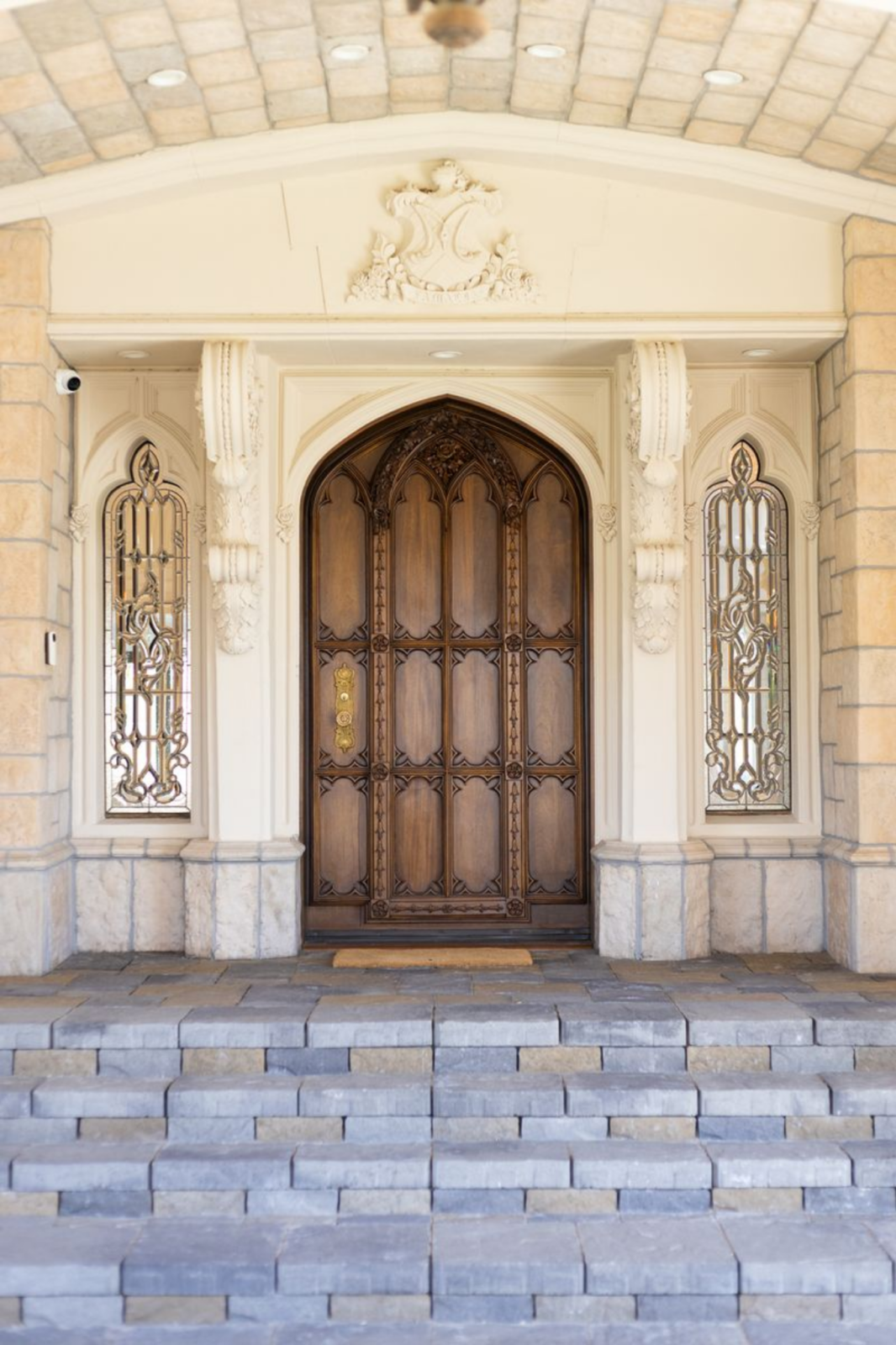 At the front door, a set of shallow stone steps leads up to a carved wooden door with a pointed arch, its surface divided into paneled sections with intricate trim.